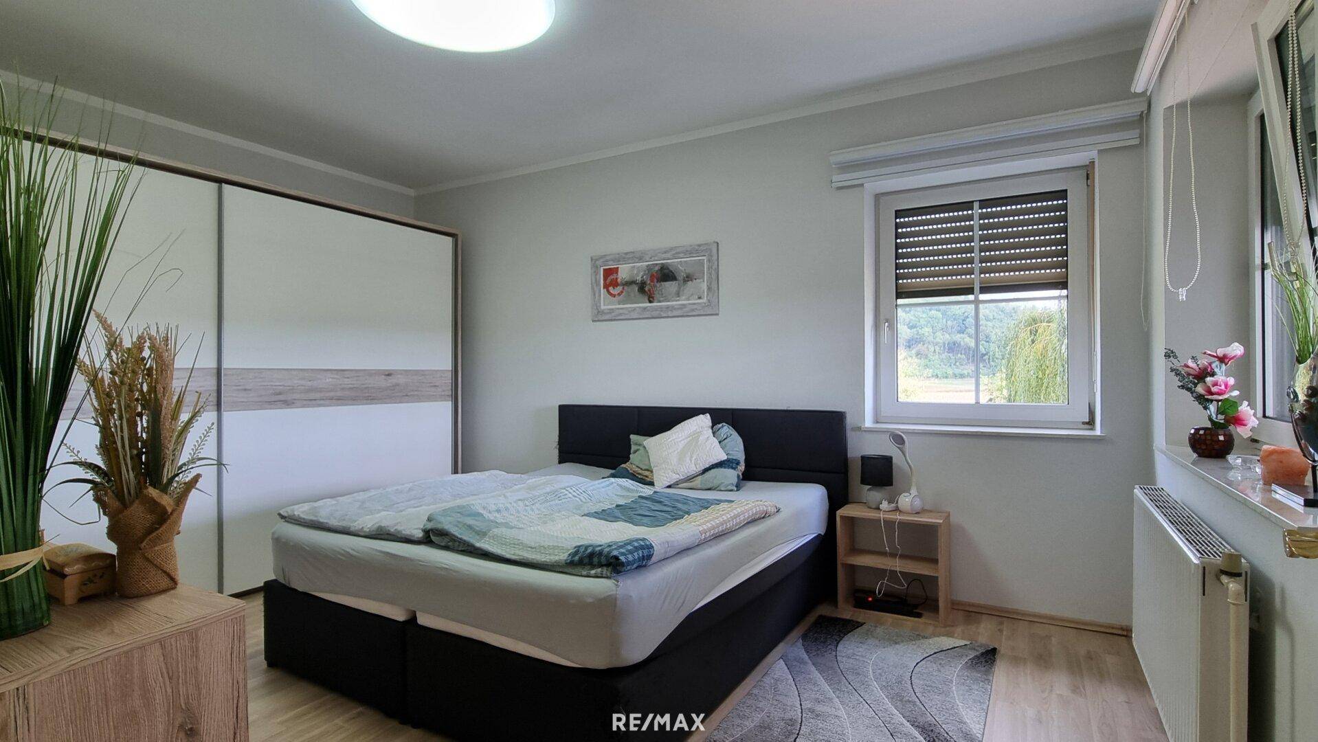 Helles Schlafzimmer mit Doppelbett, Schiebetürenschrank und Fenster mit Blick ins Grüne.