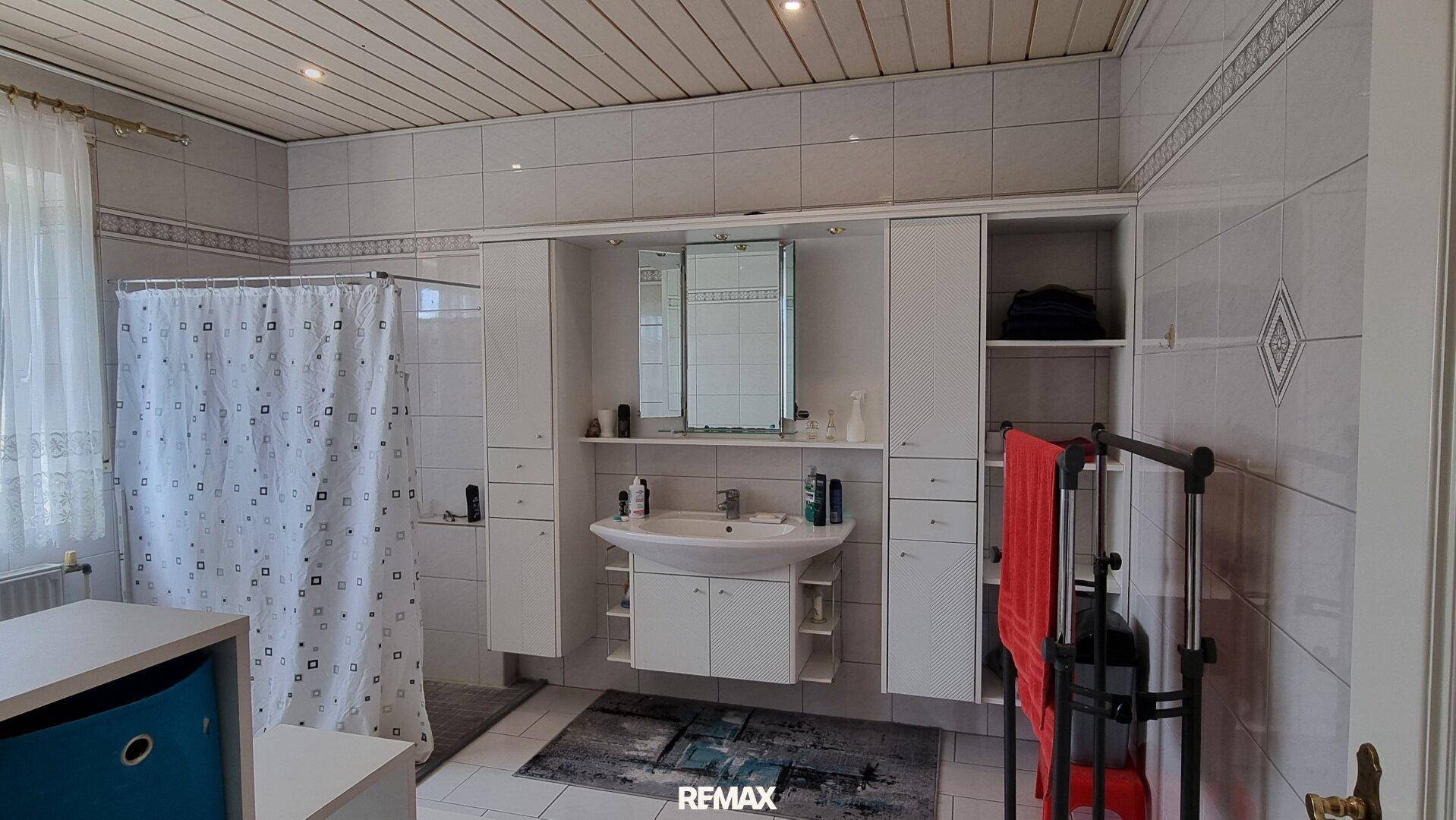 Gefliestes Badezimmer mit Waschtisch, Spiegelschrank und Duschvorhang.