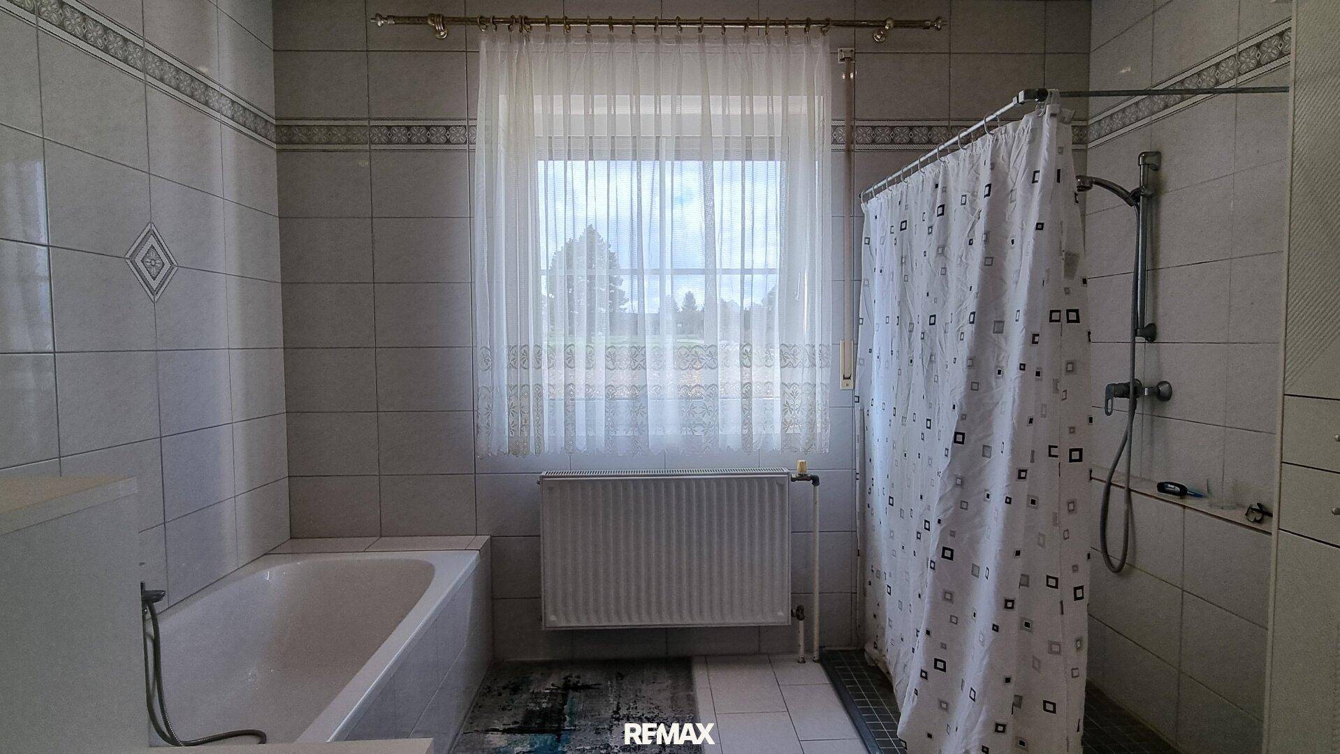 Badezimmer mit Badewanne, Duschbereich und Fenster, komplett gefliest.