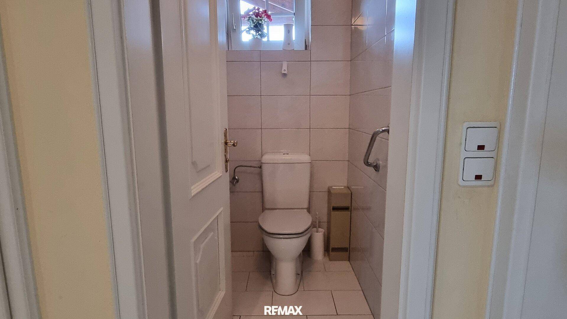 Separate Gästetoilette mit Fenster, Wand-WC und Haltegriffen für Barrierefreiheit.