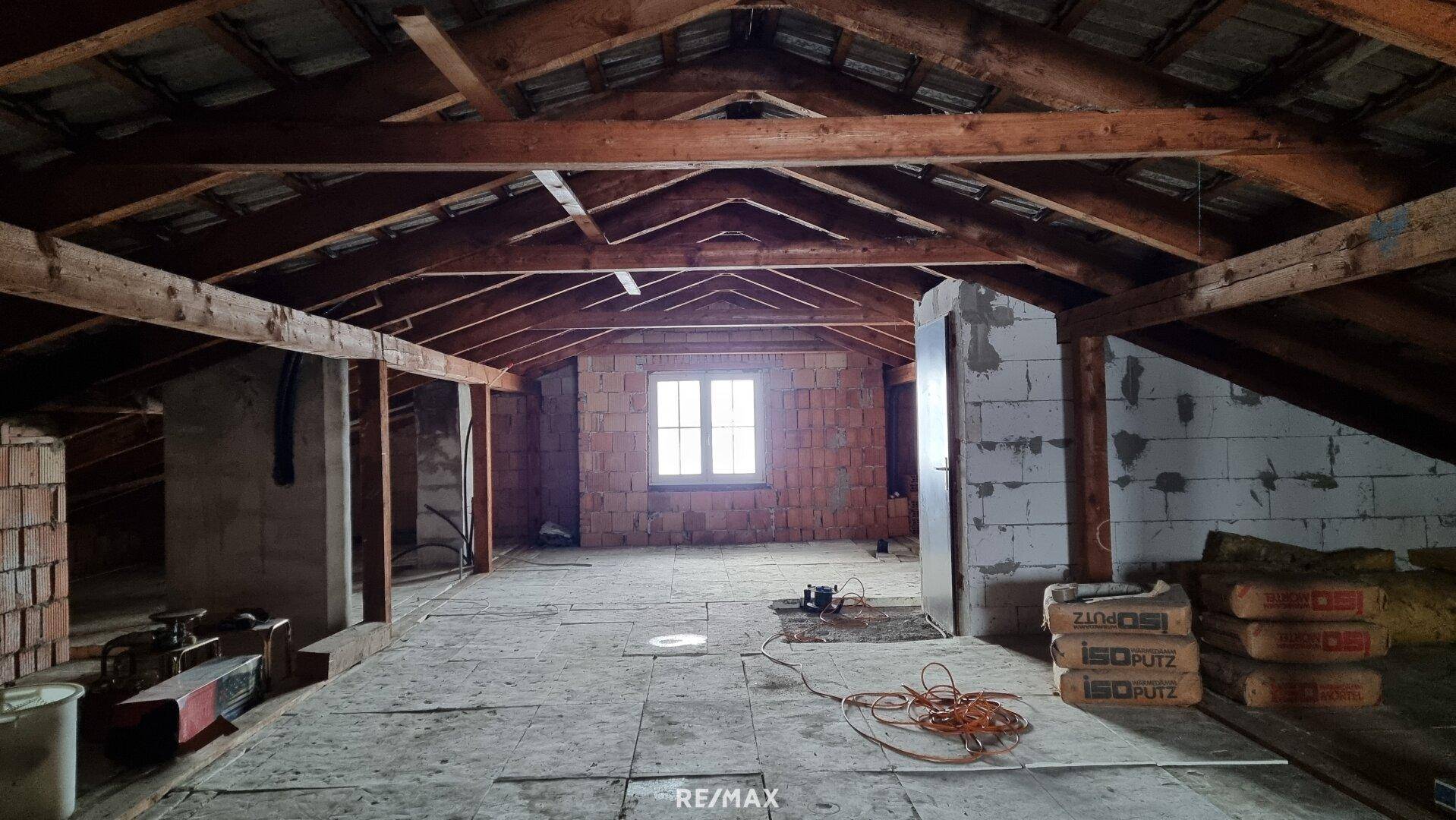Unausgebauter Dachboden mit sichtbaren Holzbalken und Fenster, bereit für Ausbau.
