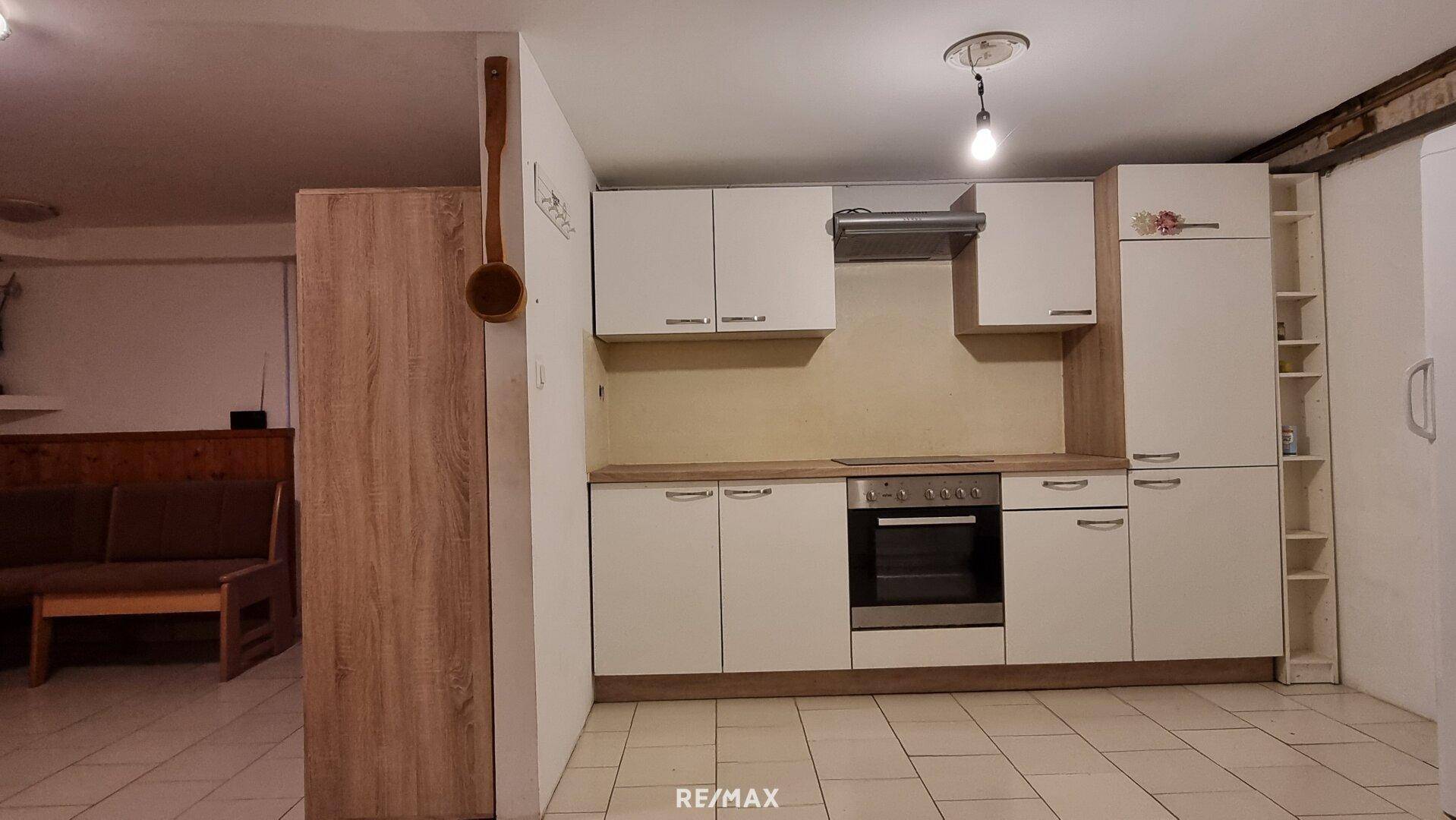 Kleine Küche im Kellerbereich mit weißen Schränken und Fliesenboden.