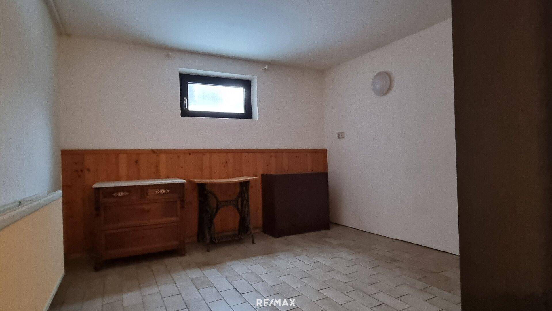 Weiterer Kellerraum mit Fliesenboden und Holzvertäfelung, mit kleinem Fenster.