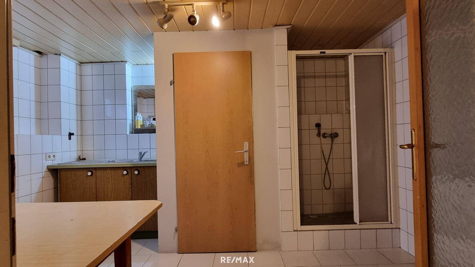 Einfaches Badezimmer im Keller mit Dusche und kleiner Küchenzeile.