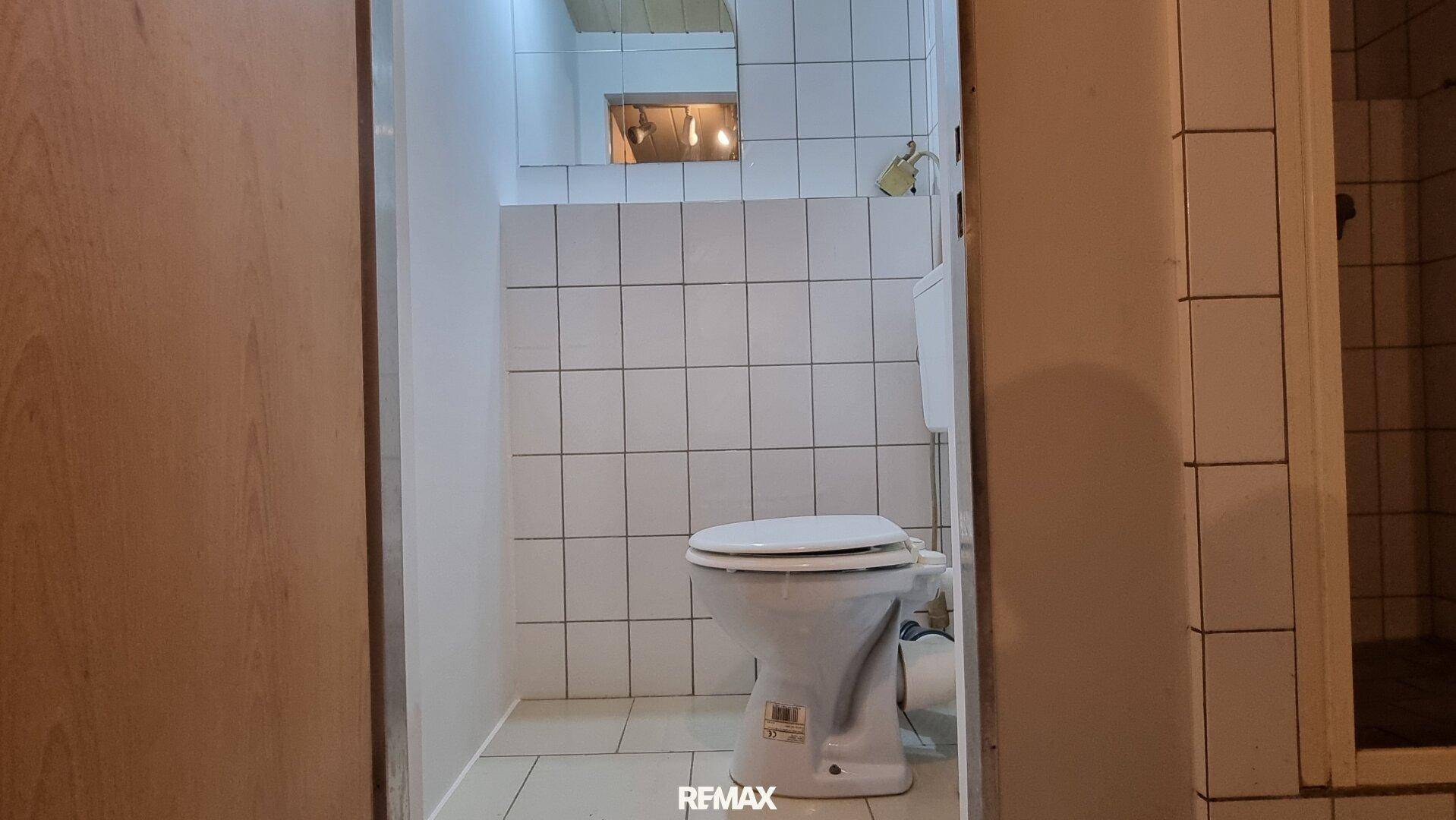 Kleines WC mit weißen Fliesen und einfacher Ausstattung, durch eine Türöffnung sichtbar.