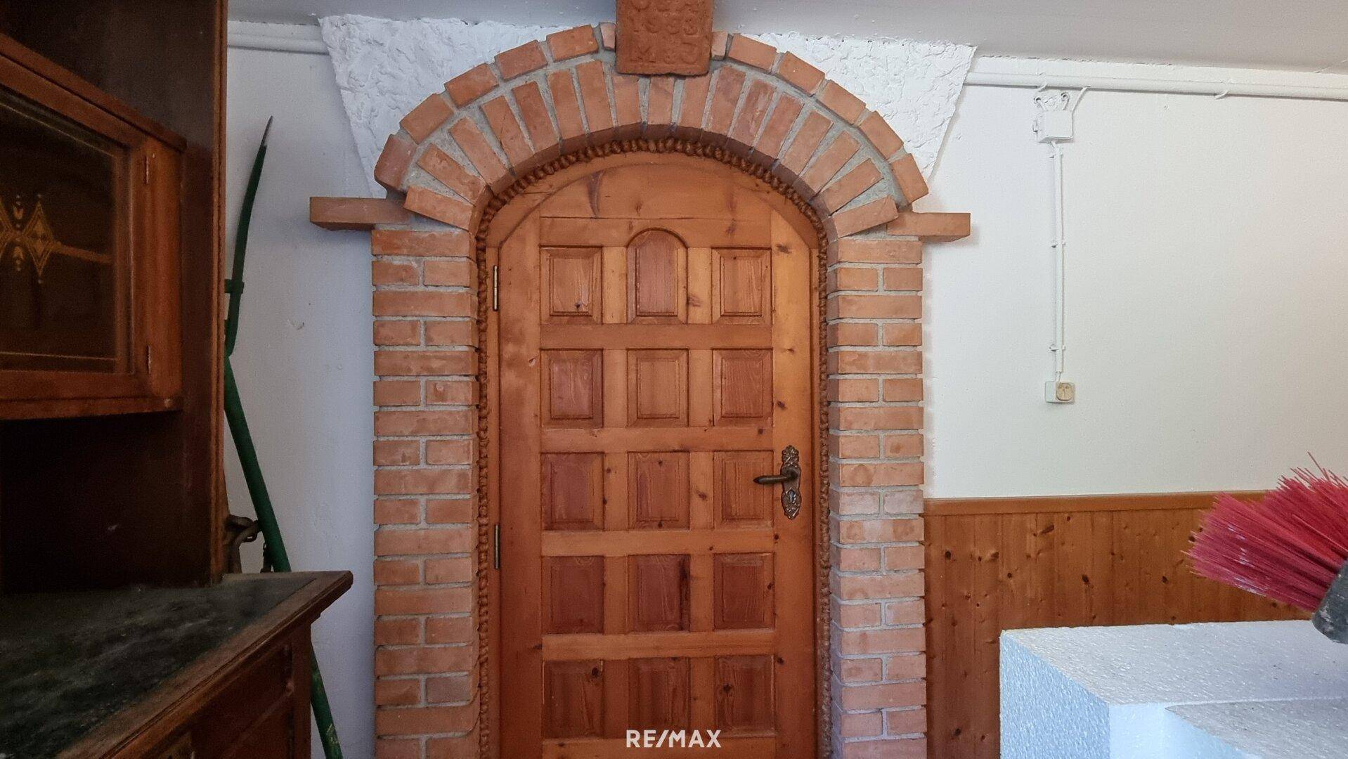 Rustikale Holztür mit Ziegelbogen im Kellerbereich, die zu einem weiteren Raum führt.