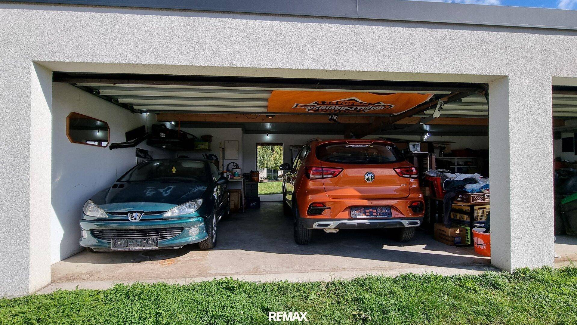Doppelgarage mit zwei Fahrzeugen und offenem Zugang, umgeben von einer Rasenfläche.