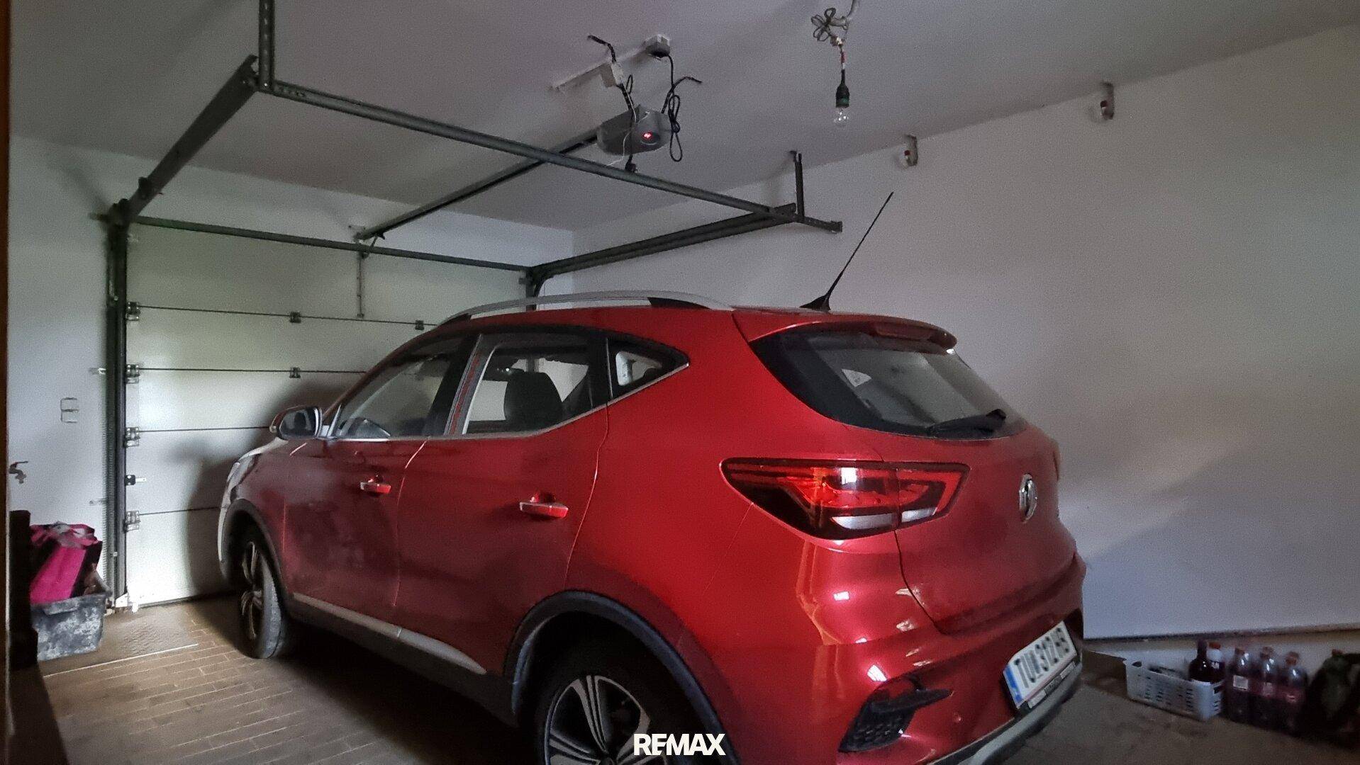 Einzelgarage mit einem geparkten Auto und automatischem Garagentor, gut beleuchtet.