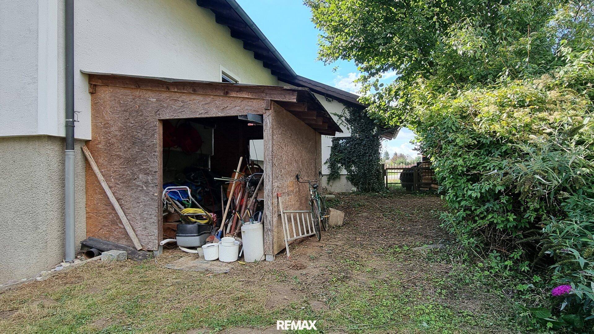 Einfacher Holzschuppen neben dem Haus für Gartengeräte und Lagerung, umgeben von Grün.