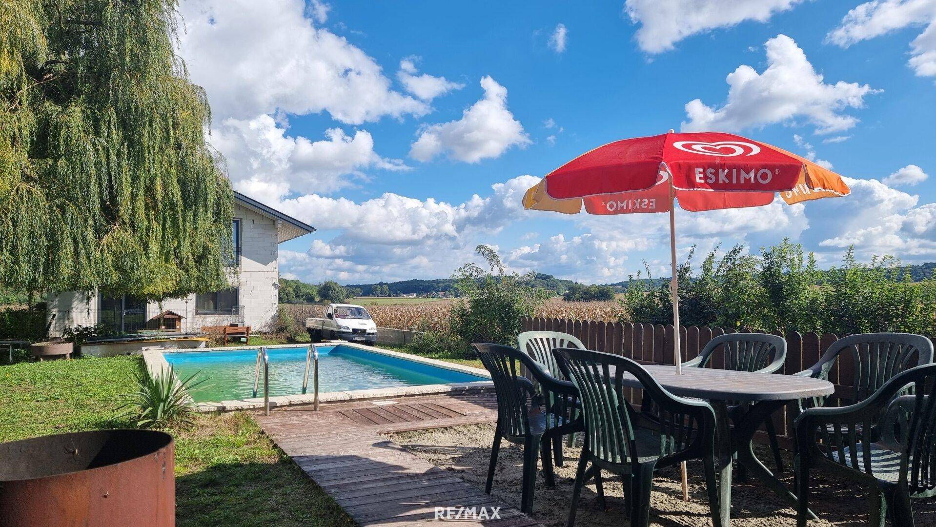 Sonniger Gartenbereich mit Swimmingpool und Essbereich im Freien, umgeben von Natur.
