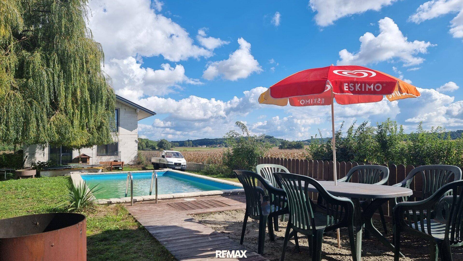 Großer Garten mit Swimmingpool, Rasenfläche und Essbereich im Freien unter einem Sonnenschirm.