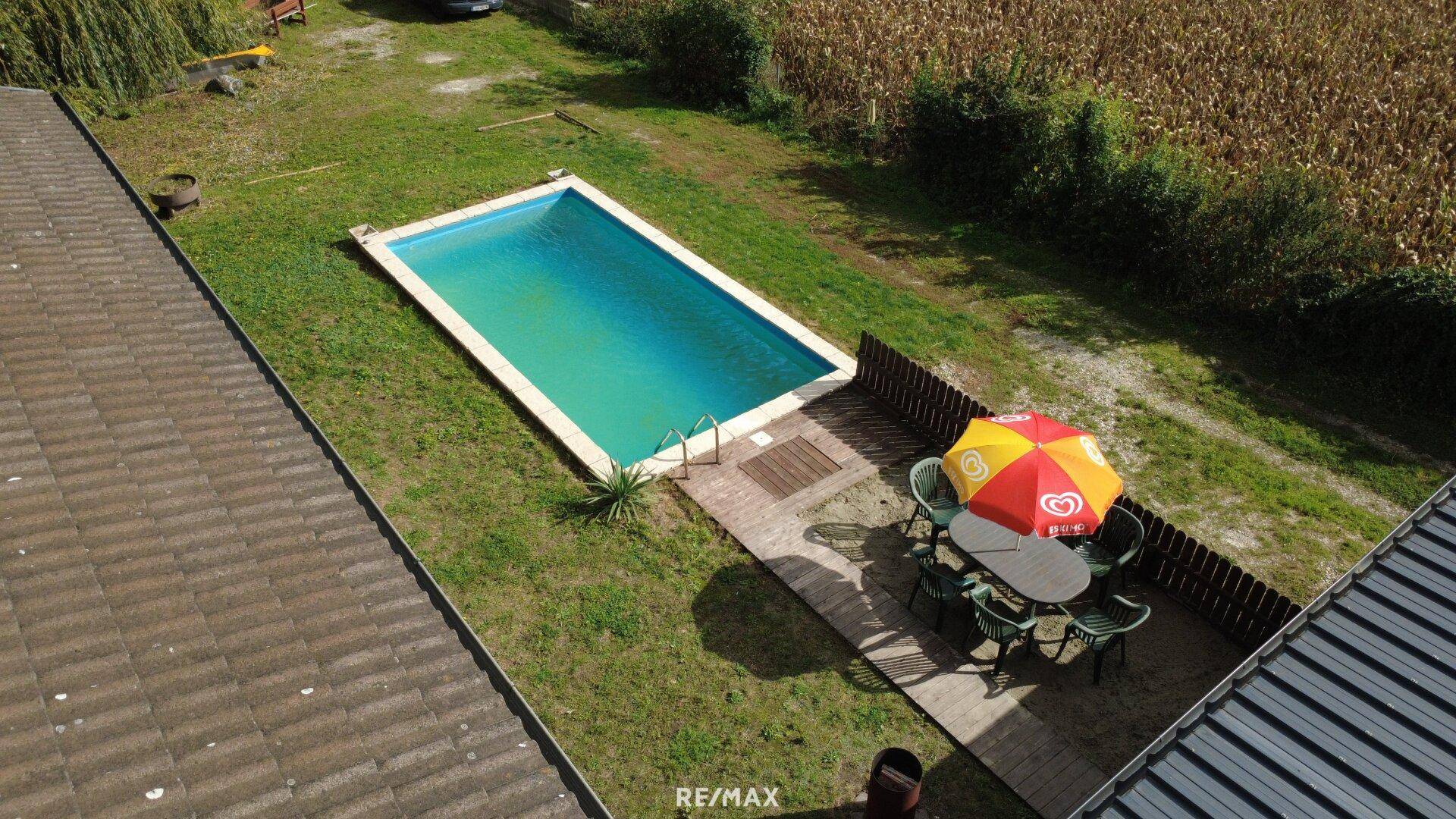 Vogelperspektive des Gartens mit Swimmingpool und Essbereich unter einem Sonnenschirm.