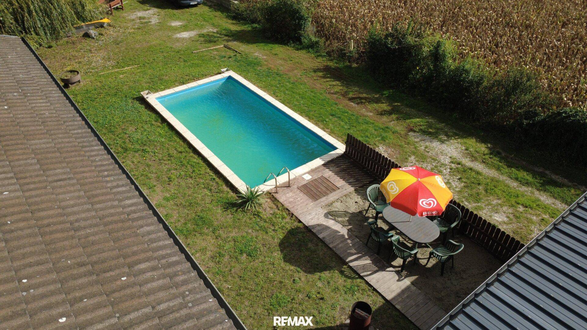 Luftaufnahme des Gartens mit Swimmingpool, Rasen und Essbereich neben einem Feld.