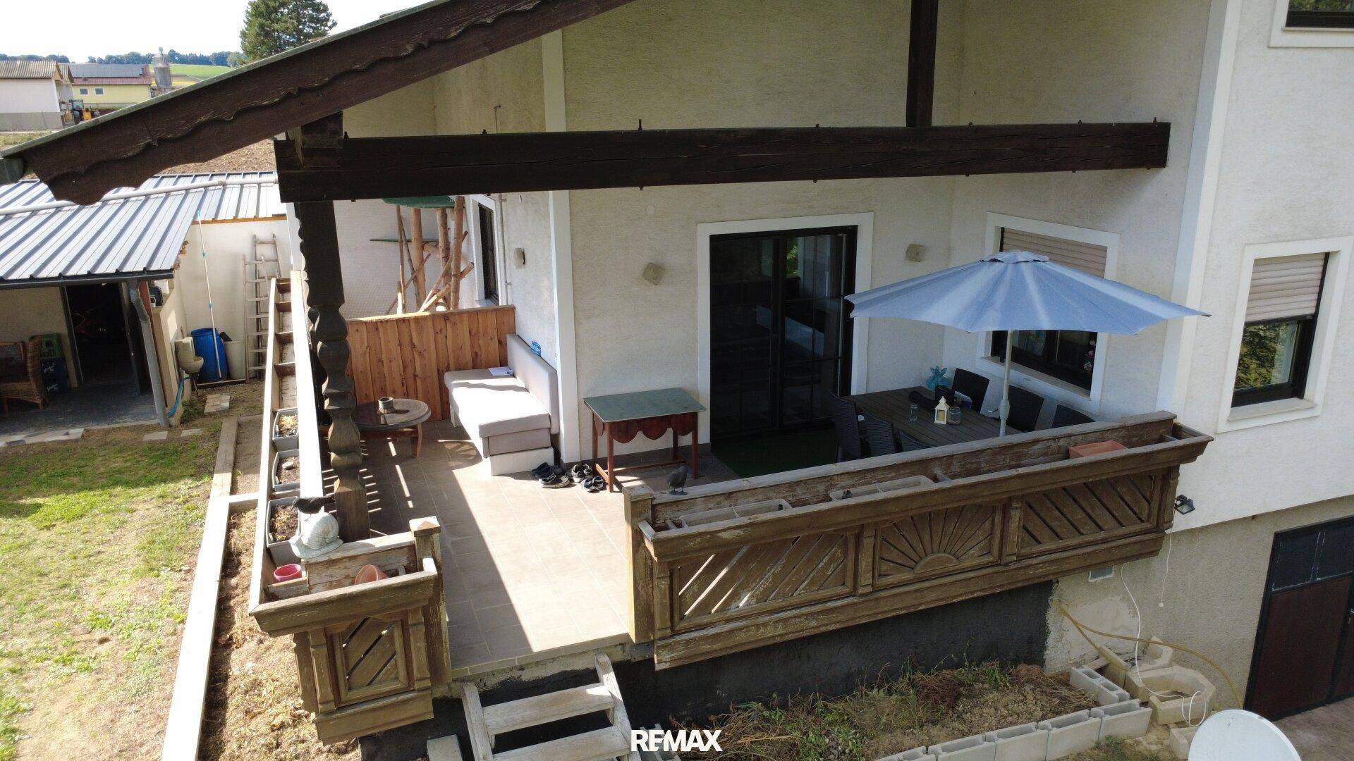 Balkon mit Holzbalken und Geländer, ausgestattet mit Sitzgelegenheiten und Sonnenschirm.