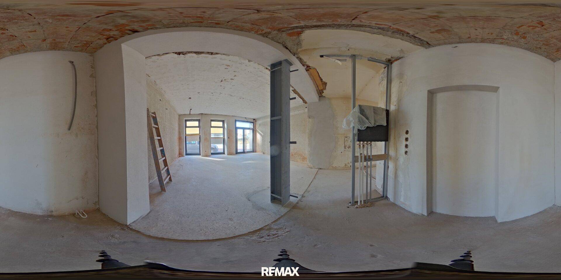 Panoramaansicht eines großen Geschäftsraums im Rohbau mit Aufzugsschacht und Leiter.