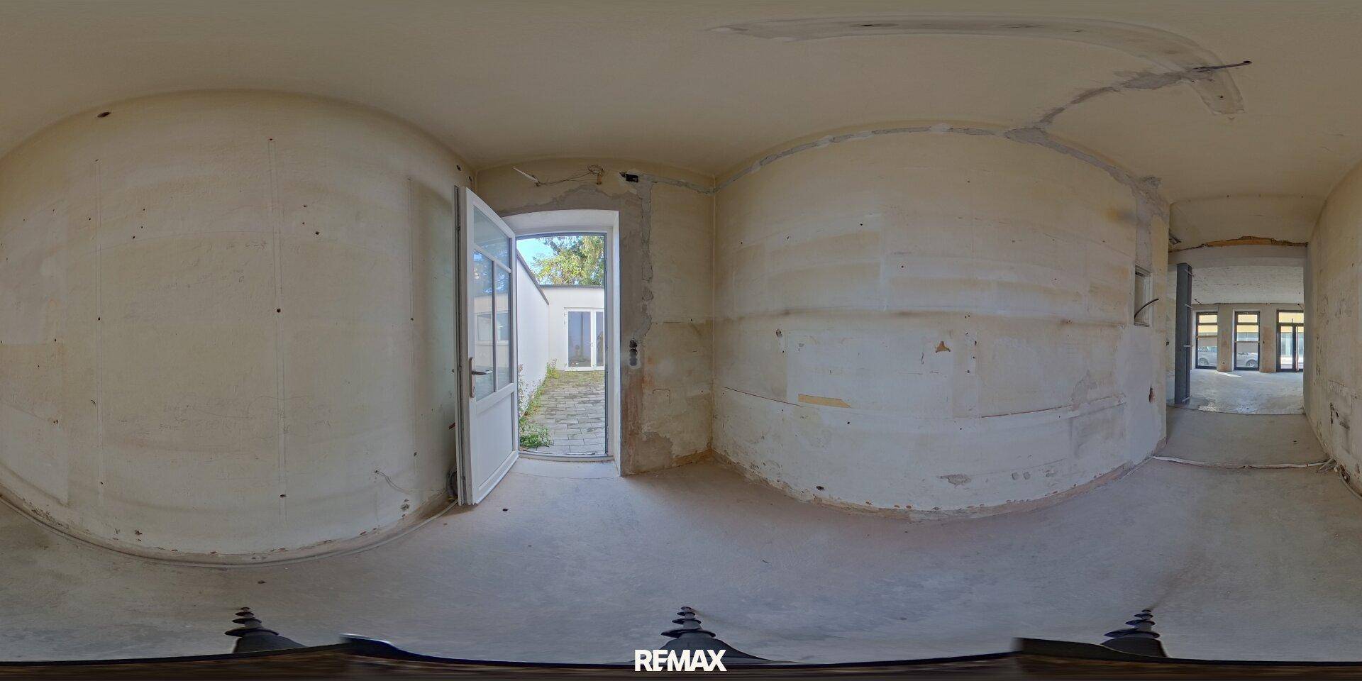 Panoramaansicht eines Rohbauraums mit einer offenen Tür, die zu einem Außenbereich führt.