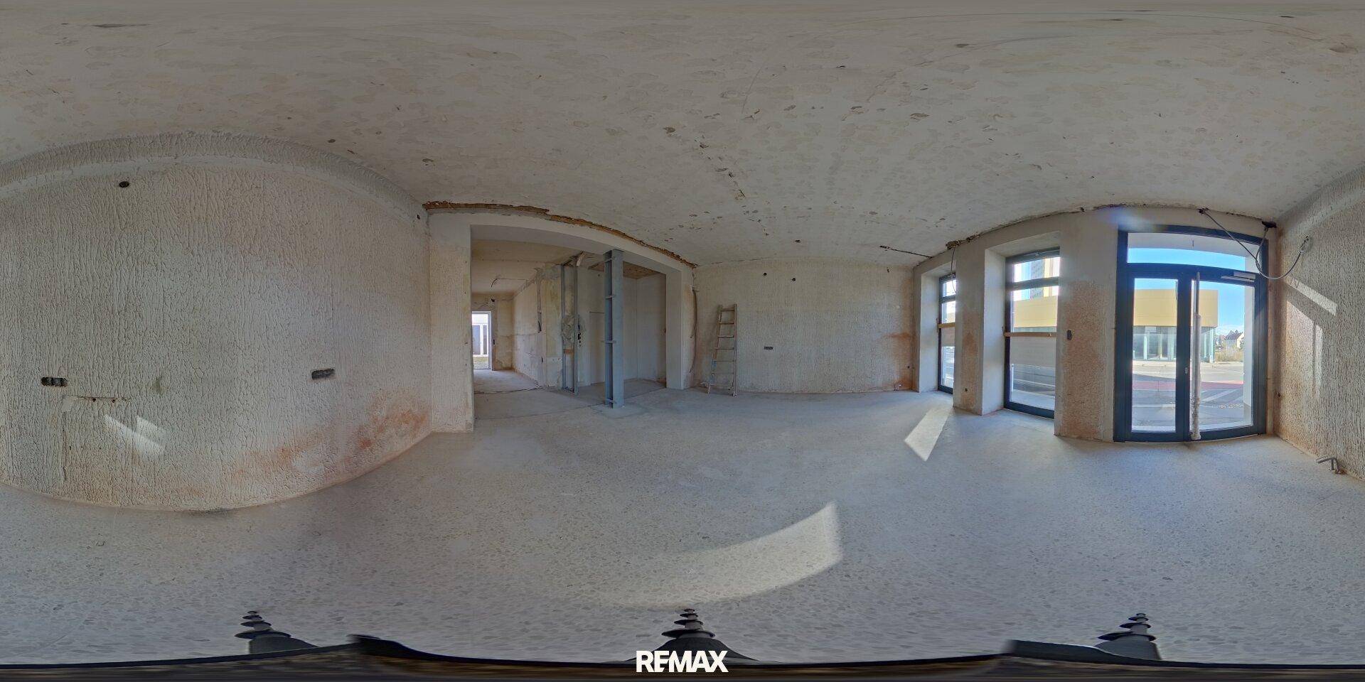 Panoramaansicht eines weitläufigen Geschäftsraums im Rohbau mit vielen Fenstern und Durchgängen.