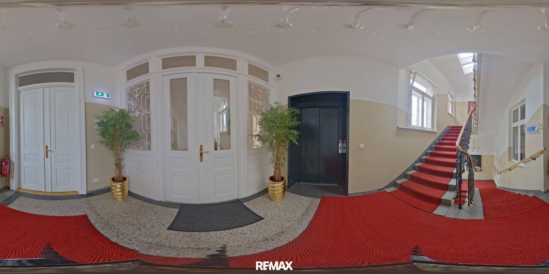 Panoramaansicht des Eingangsbereichs mit Aufzug, Treppe und verzierten Türen.