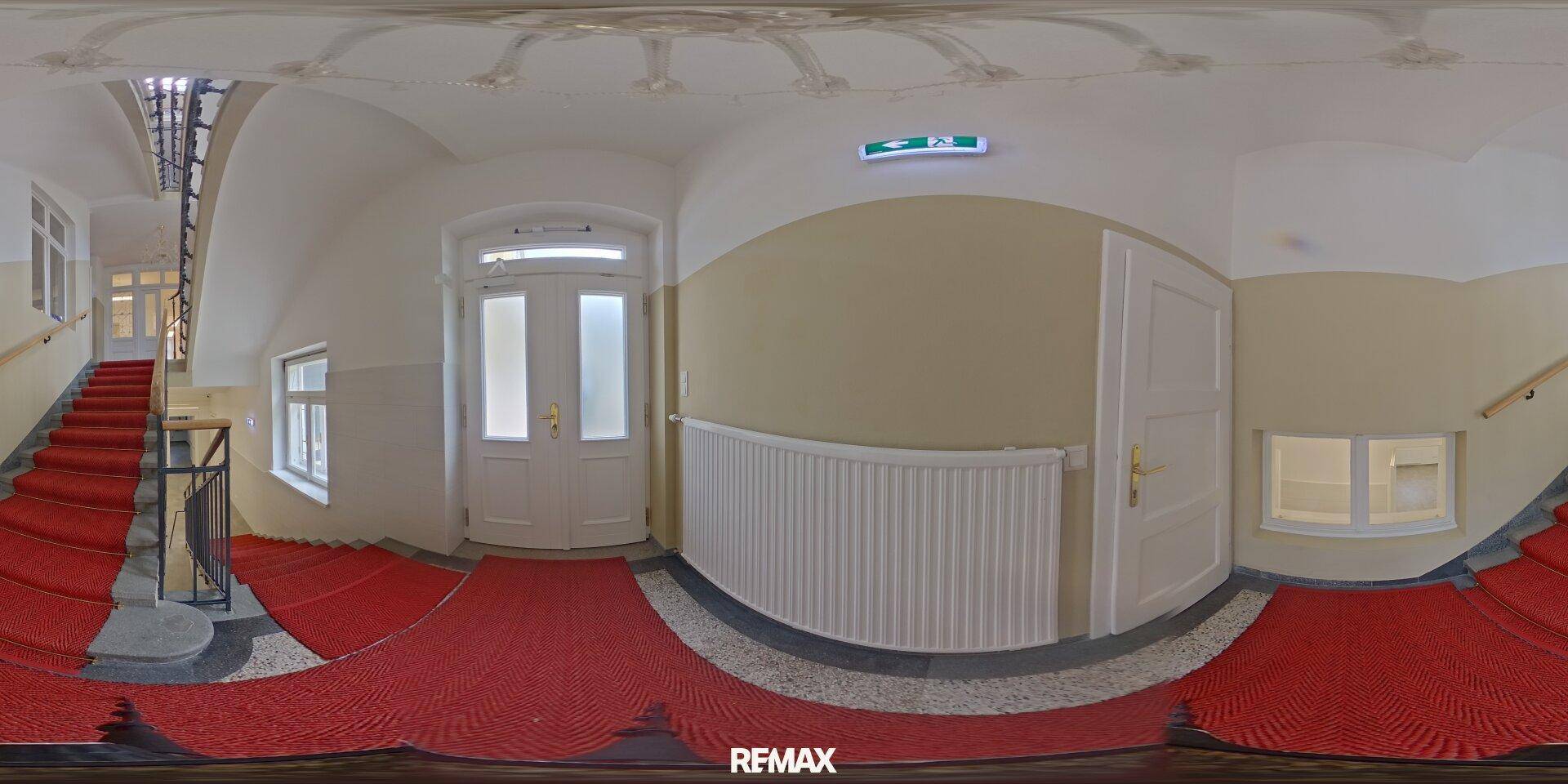 Panoramaansicht des Treppenhauses mit rotem Teppich, Geländer und dem Eingangsbereich.