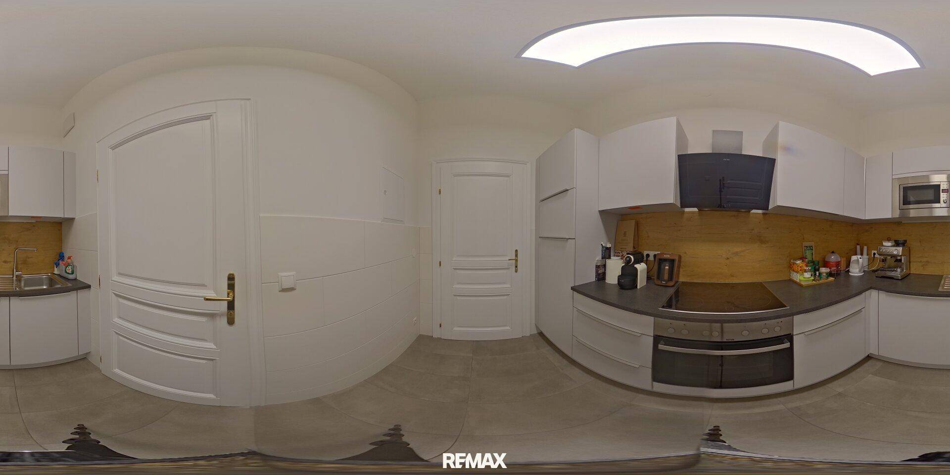Panoramaansicht einer modernen Küche mit weißen Schränken, dunkler Arbeitsplatte und Holzrückwand.