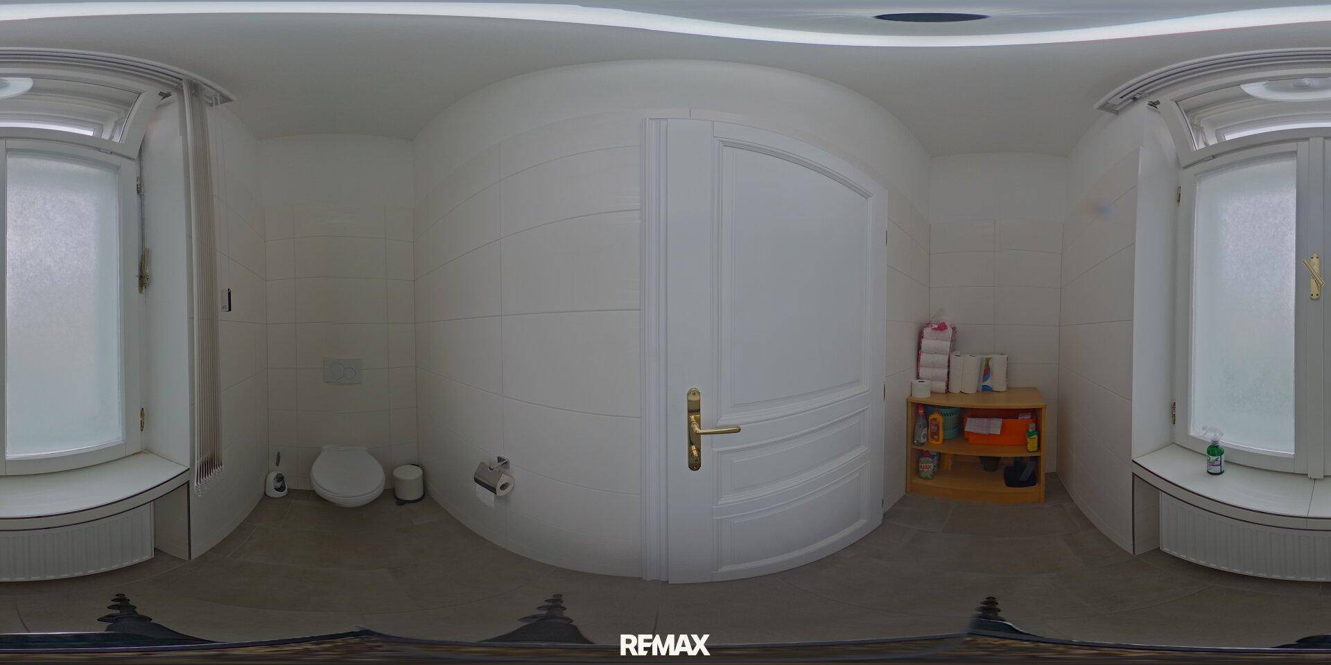 Badezimmer mit Toilette, Fenster für natürliches Licht und einem kleinen Holzregal.
