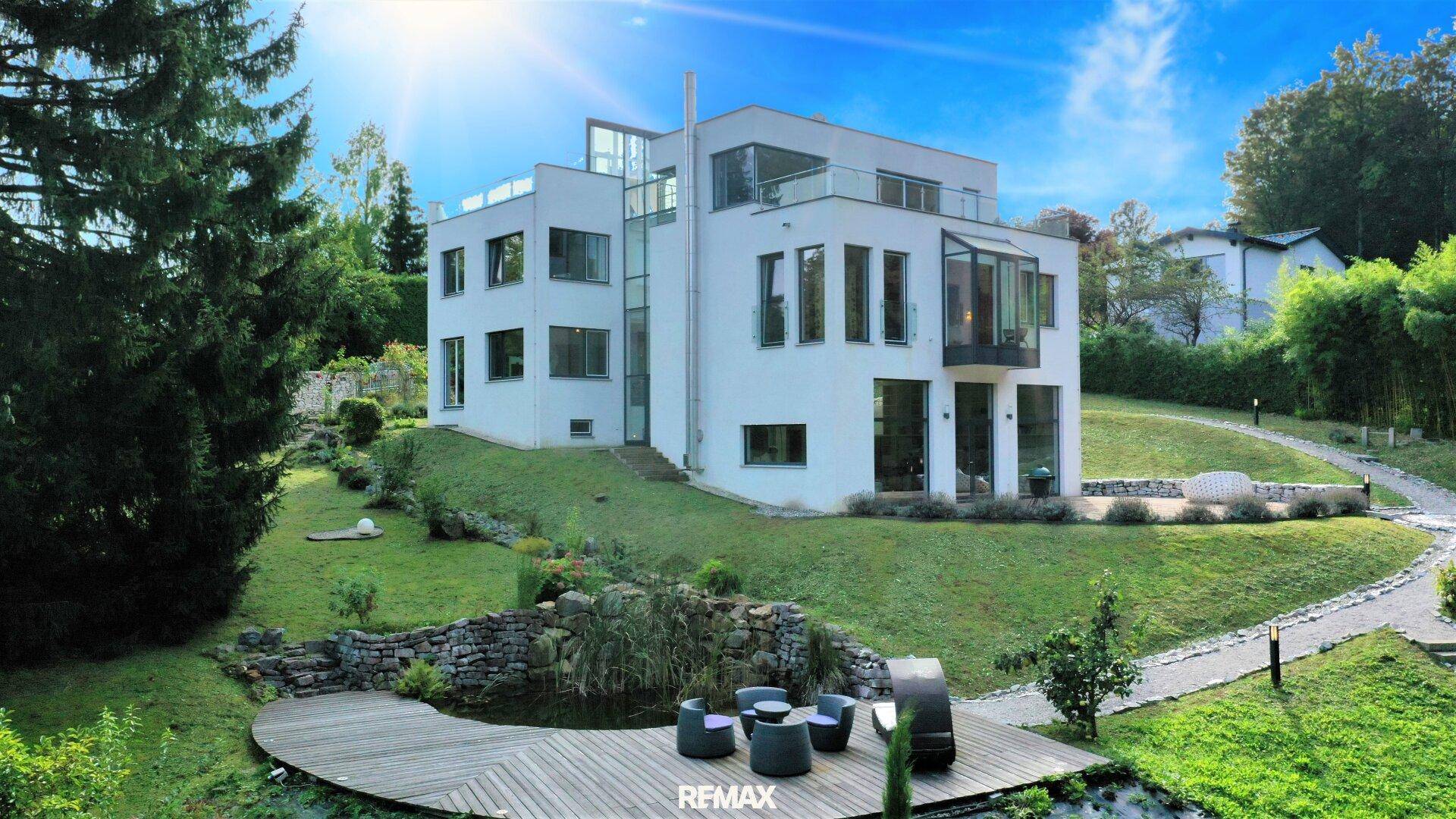 Elegante moderne Villa mit weitläufigem Garten, Teich und sonniger Holzterrasse.