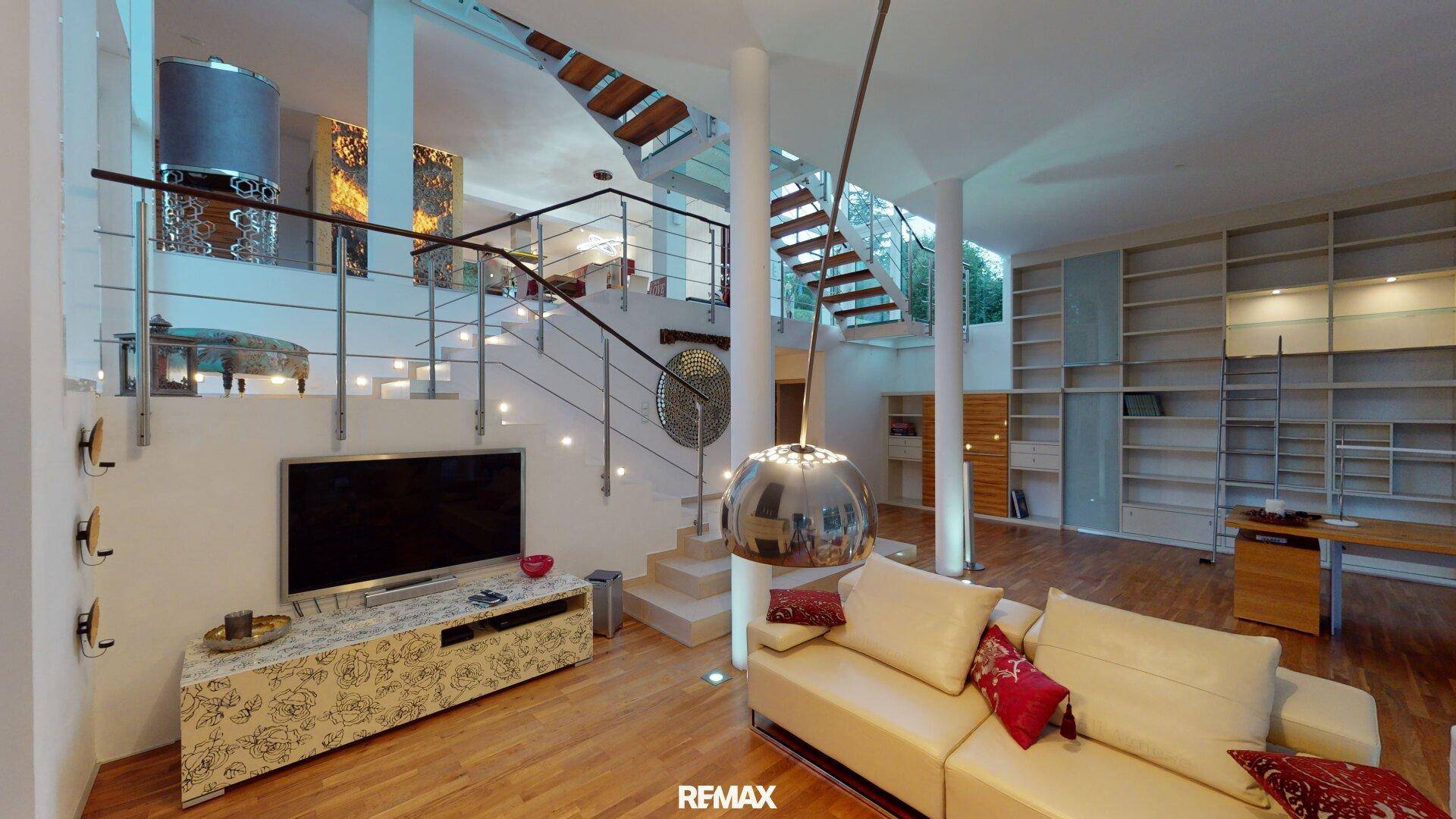 Gemütlicher Wohnbereich mit Sofa, Fernseher und Blick auf die moderne Treppenkonstruktion.