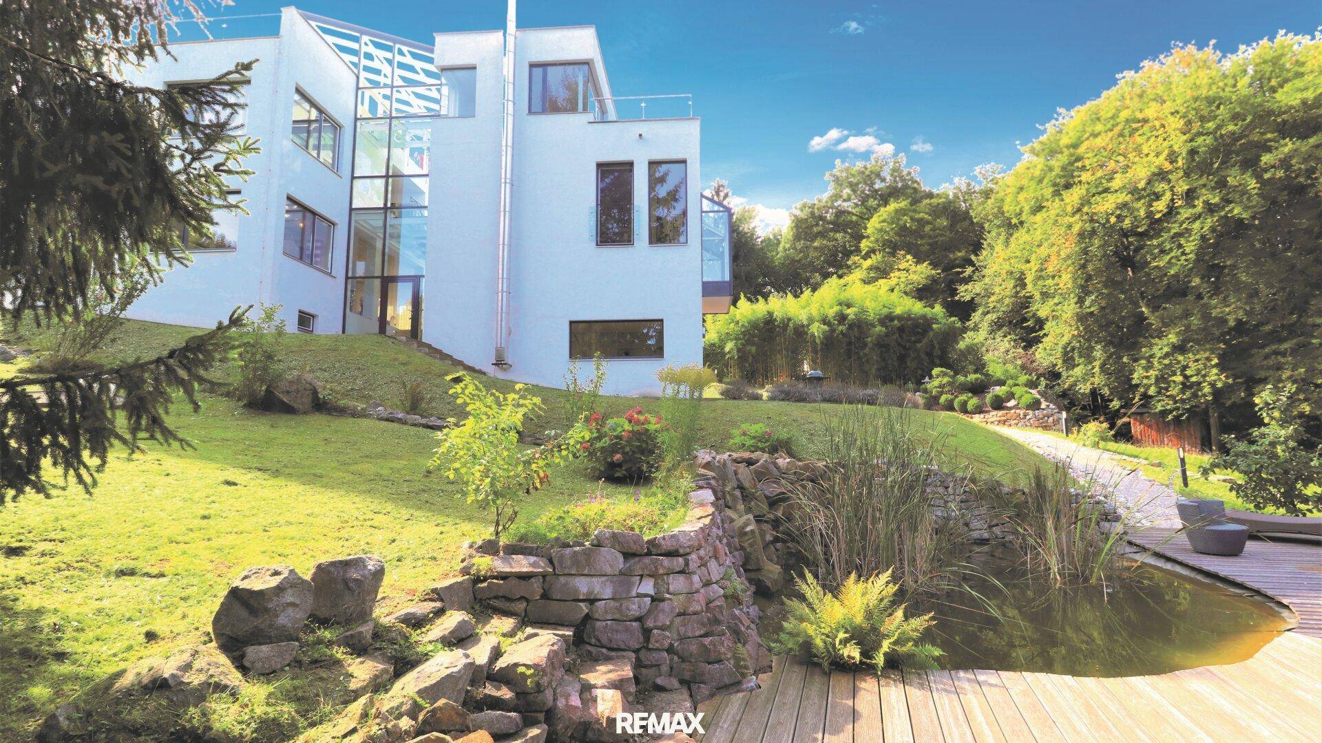 Moderne Villa mit weitläufigem Garten, Teich und Steingarten, umgeben von üppigem Grün.