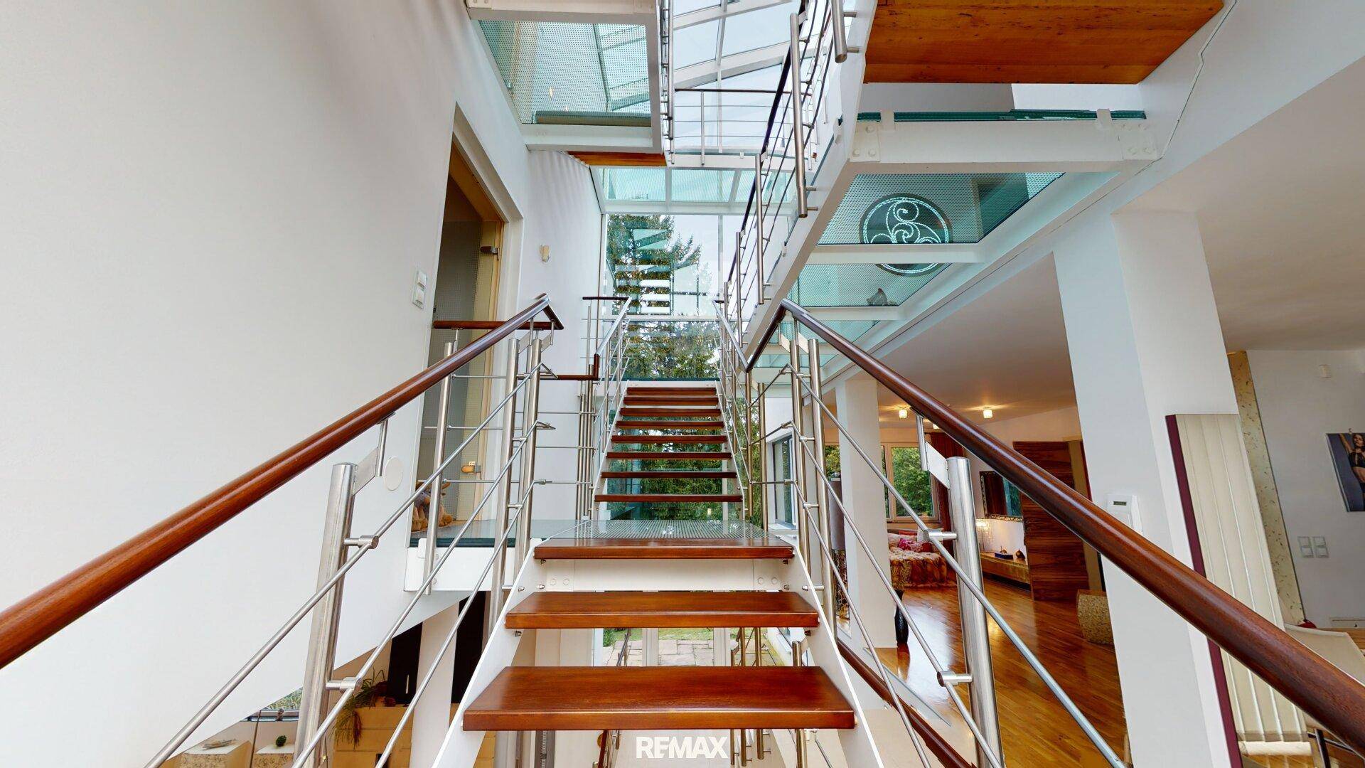 Elegante Holztreppe mit Glasgeländer und viel Tageslicht, die die verschiedenen Ebenen verbindet.
