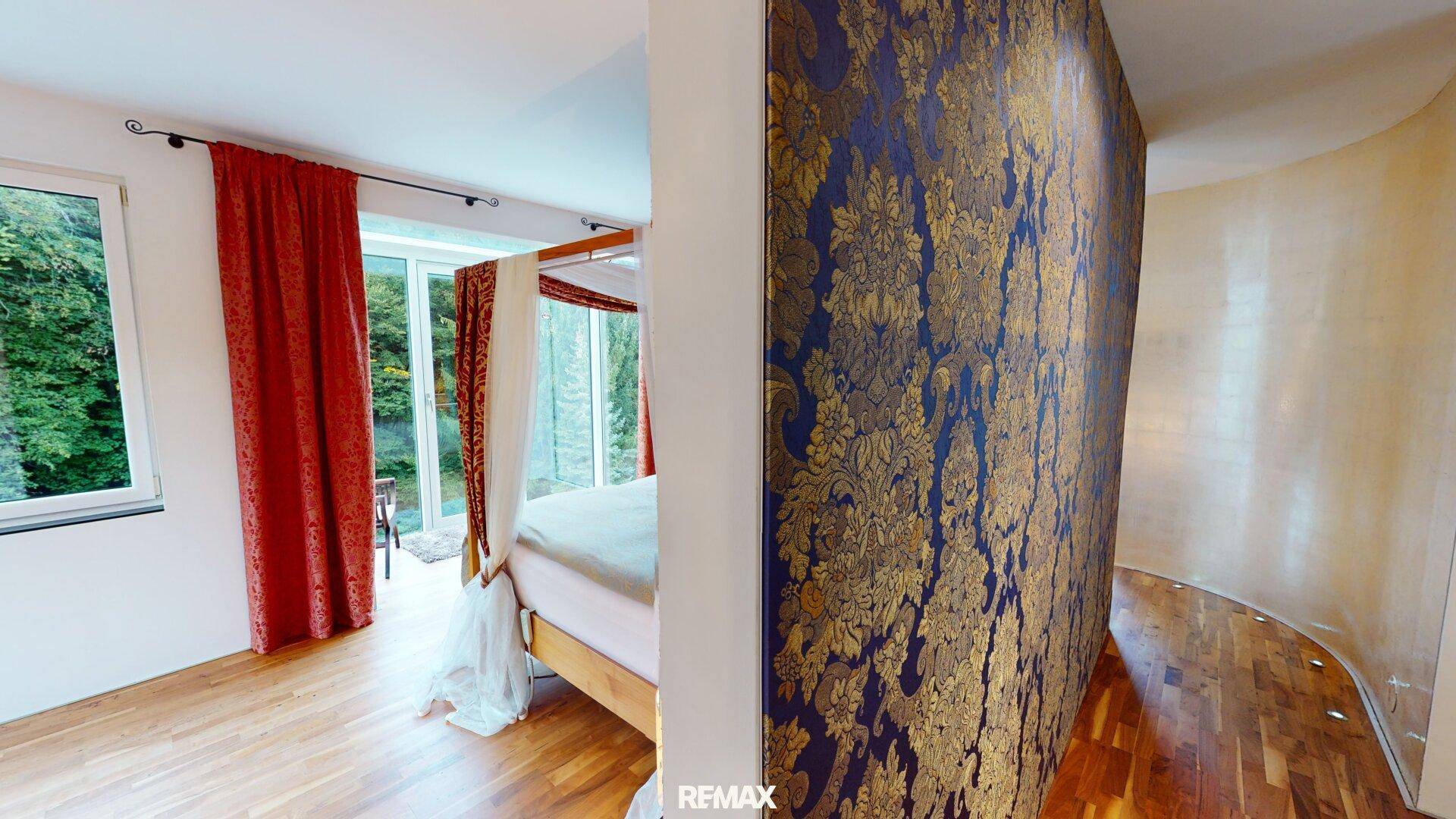 Schlafzimmer mit Himmelbett, Holzboden und dekorativer Wandtapete in Gold und Blau.