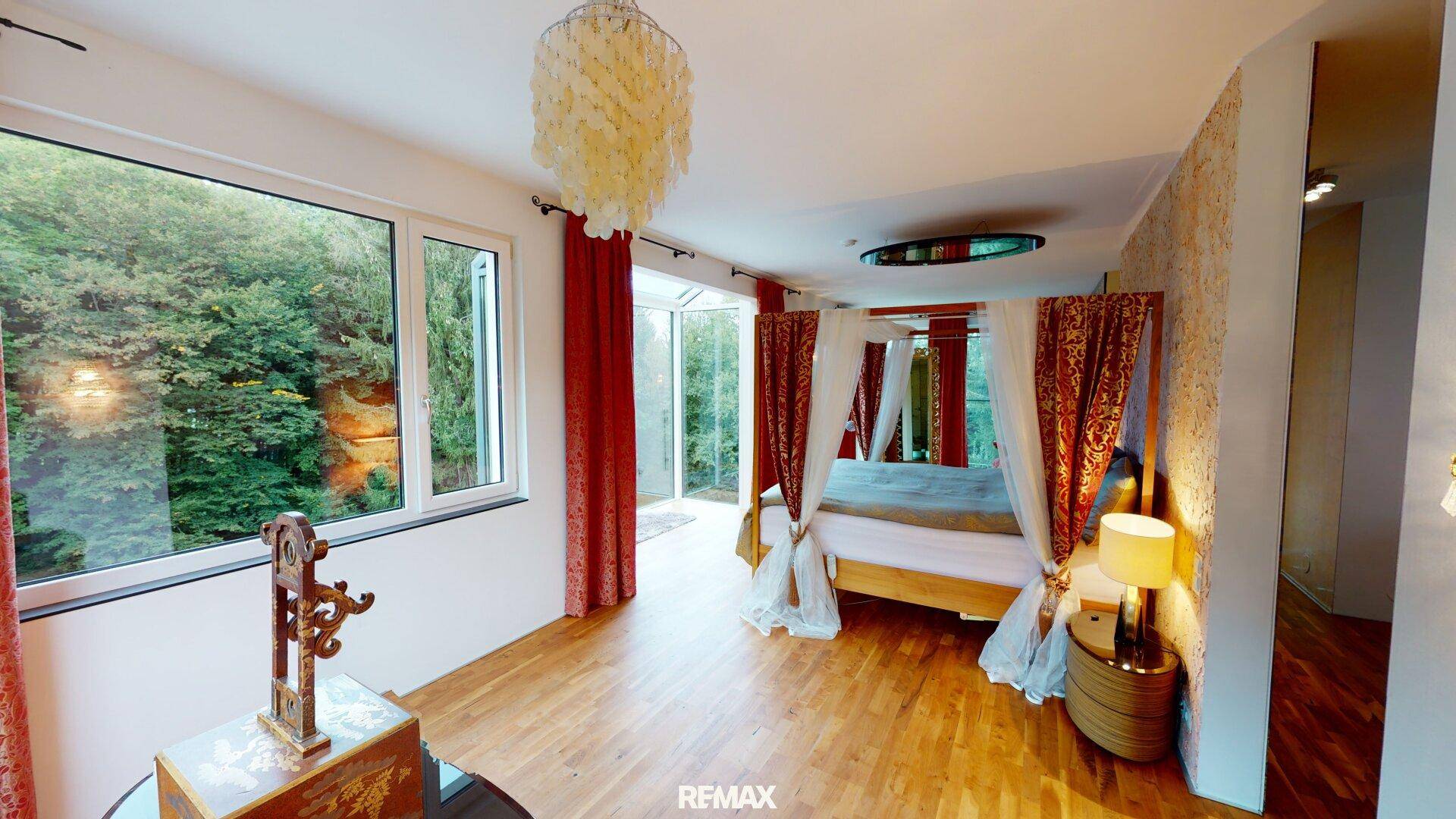 Helles Schlafzimmer mit Himmelbett, Holzboden und großen Fenstern mit Blick ins Grüne.