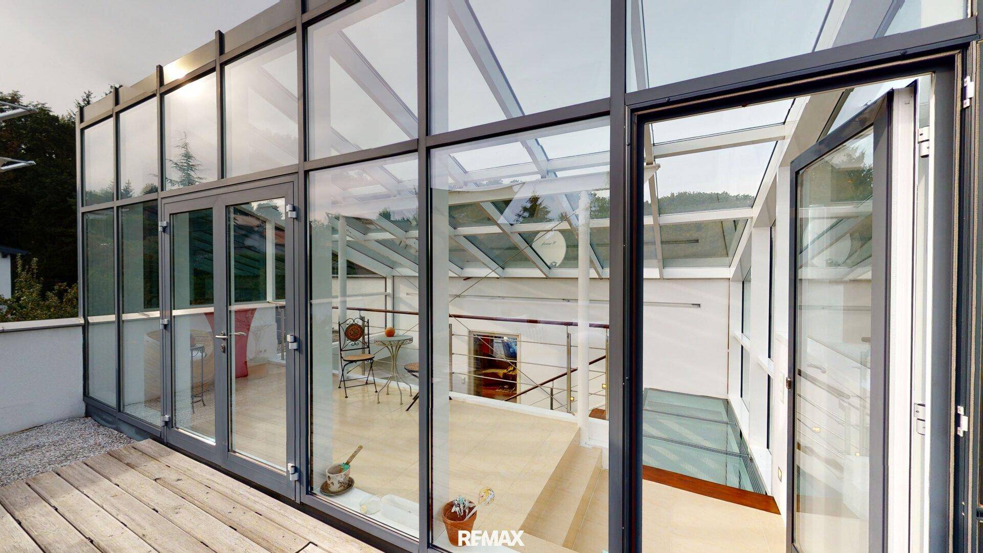Moderne Dachterrasse mit Holzdeck und verglastem Aufbau, der viel Licht hereinlässt.