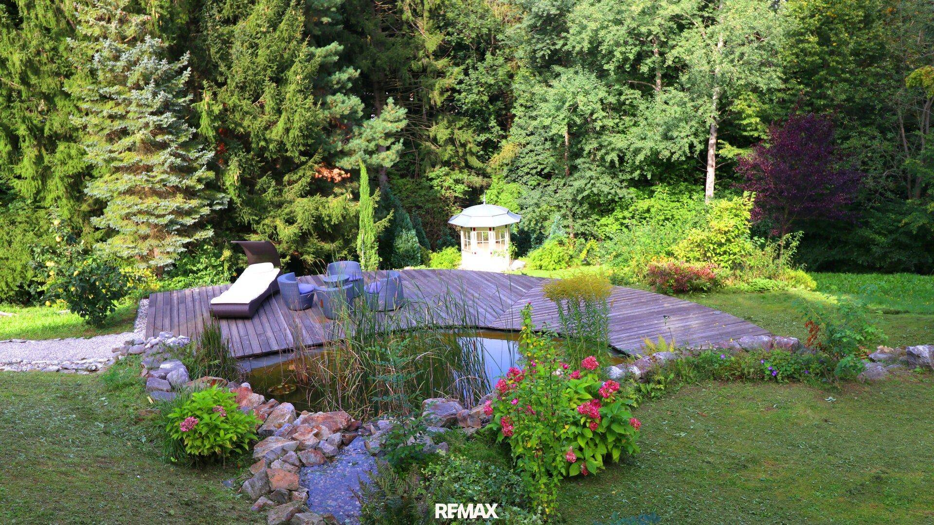 Wunderschöner, weitläufiger Garten mit Teich, Holzdeck, Sitzgelegenheiten und üppiger Vegetation.