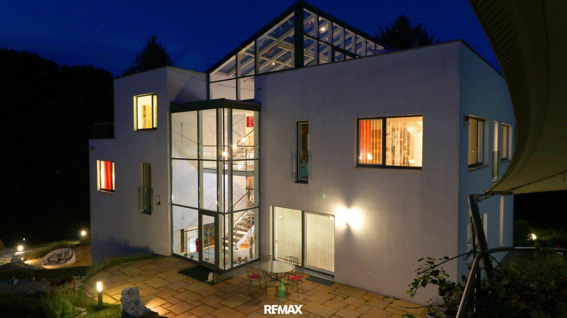 Moderne Architektur bei Nacht mit Glasanbau, Terrasse und beleuchtetem Außenbereich.