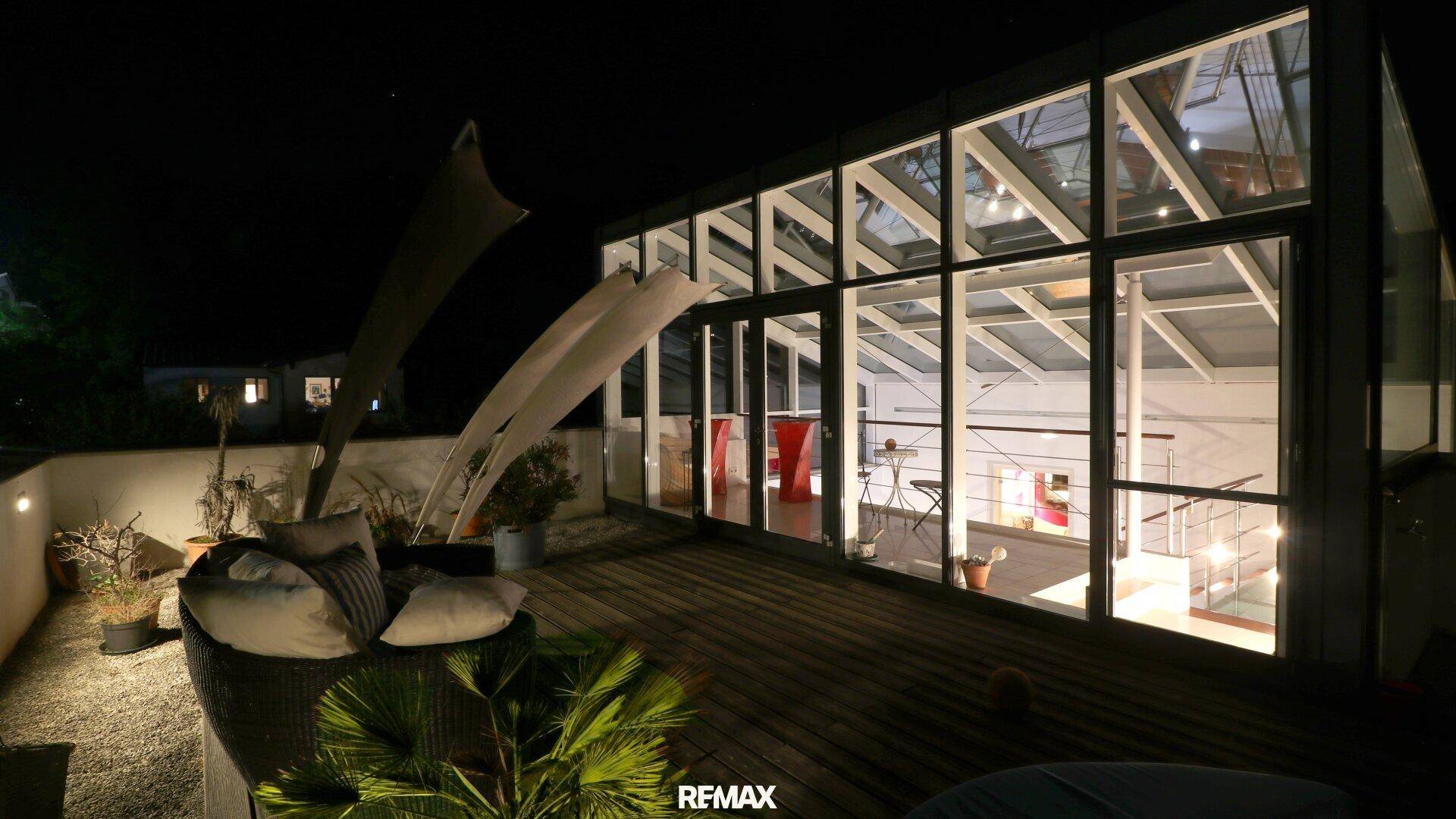 Geräumige Dachterrasse mit gemütlichen Sitzgelegenheiten und angrenzendem Wintergarten bei Nacht.