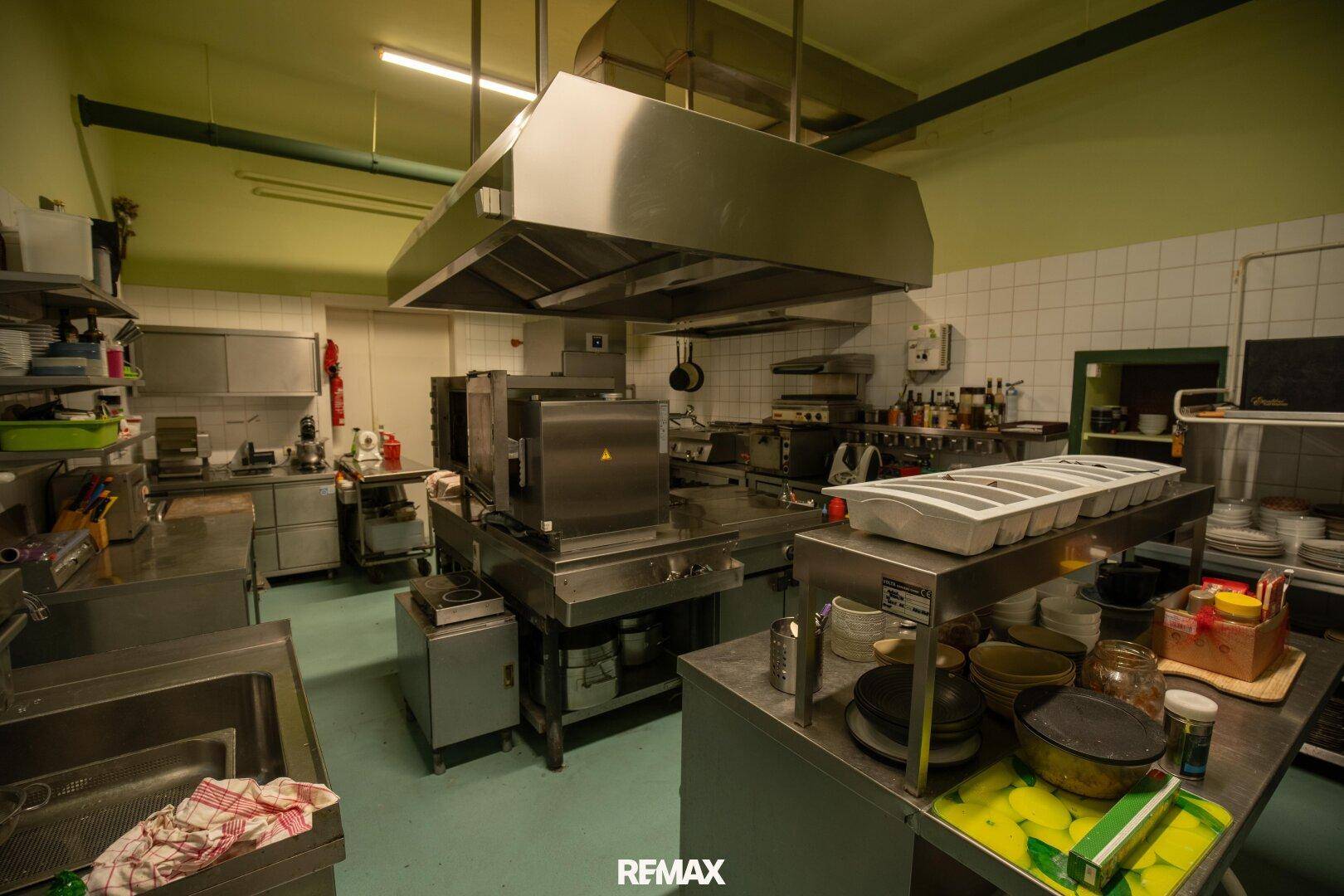 Große, professionelle Edelstahlküche mit Dunstabzugshaube und zahlreichen Arbeitsflächen für den Gastronomiebetrieb.