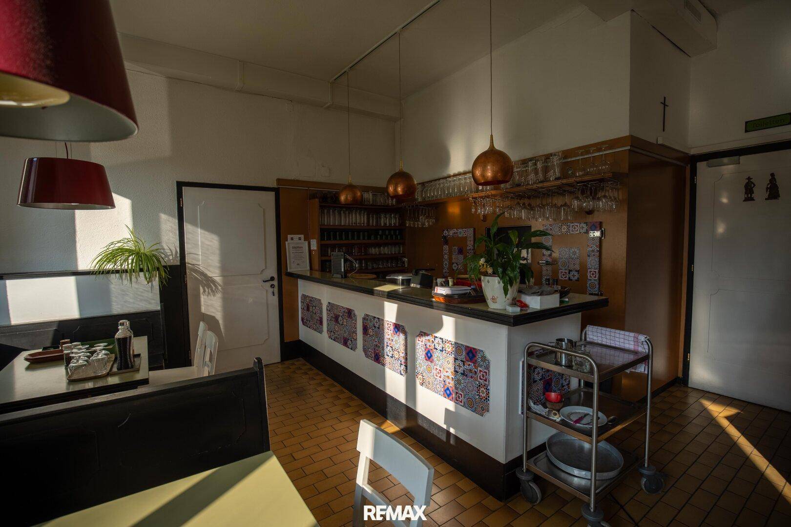 Heller Barbereich eines Restaurants mit gefliestem Boden und bunten Dekorelementen an der Theke.