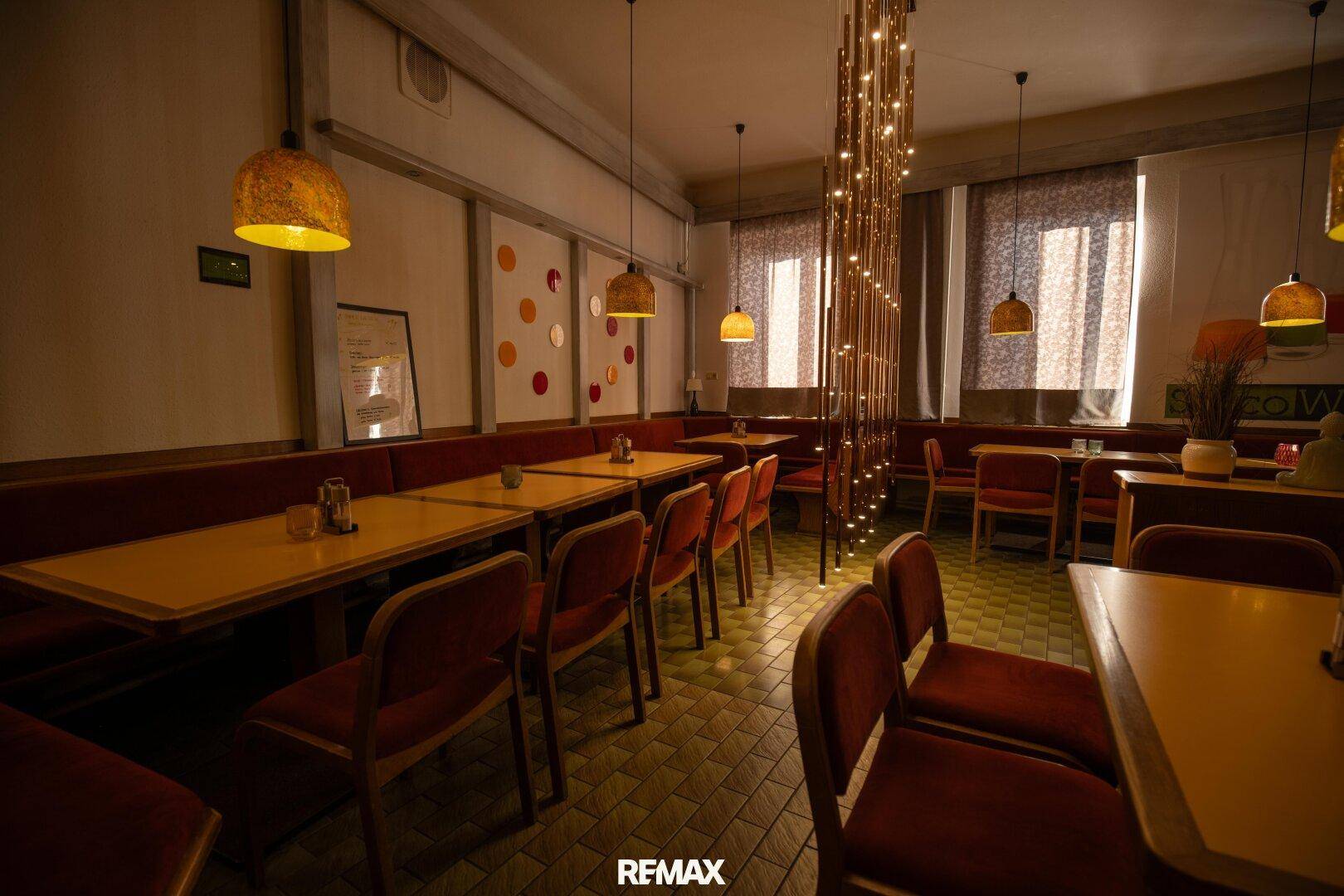 Einladender Restaurantbereich mit mehreren Tischen, roten Stühlen und gemustertem Fliesenboden.