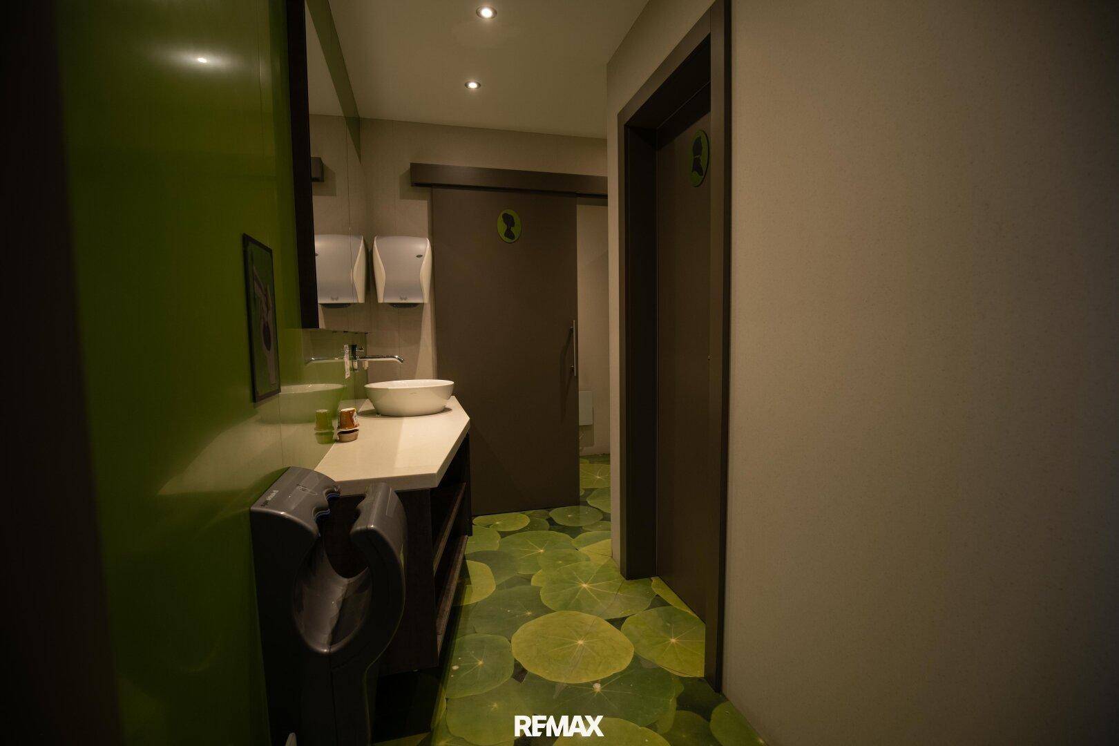 Moderner Toilettenbereich mit grünen Wänden und auffälligem Bodenmuster, das Seerosenblätter darstellt.