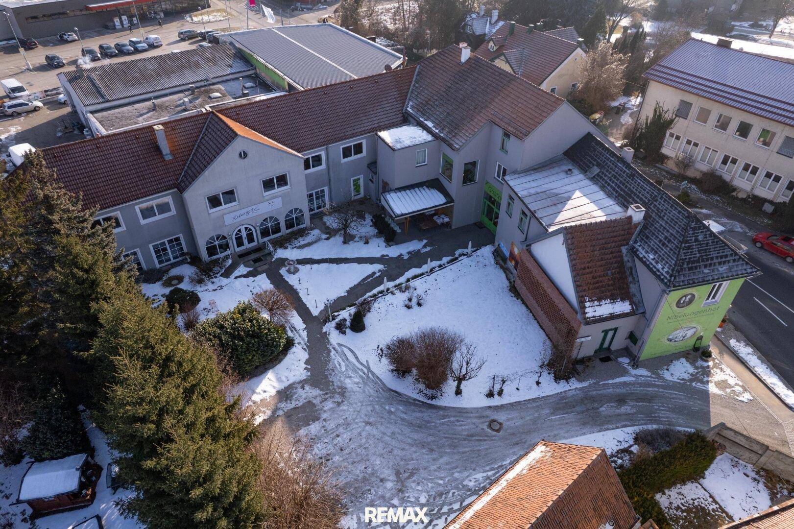 Winterliche Luftaufnahme des Gebäudekomplexes mit verschneitem Innenhof und umliegenden Bäumen.