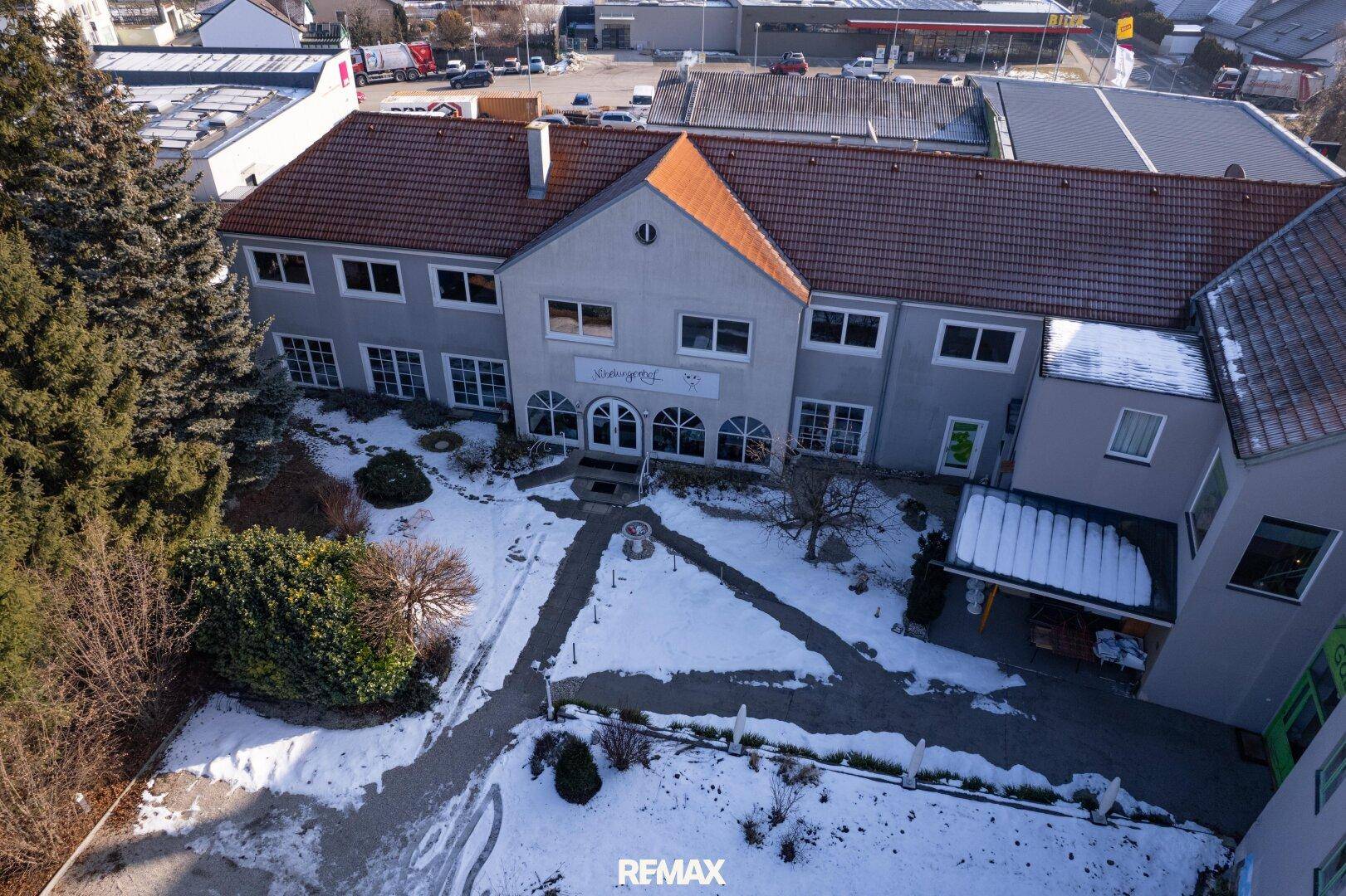Winterliche Luftaufnahme des Haupteingangs des Gebäudekomplexes mit verschneitem Vorplatz.