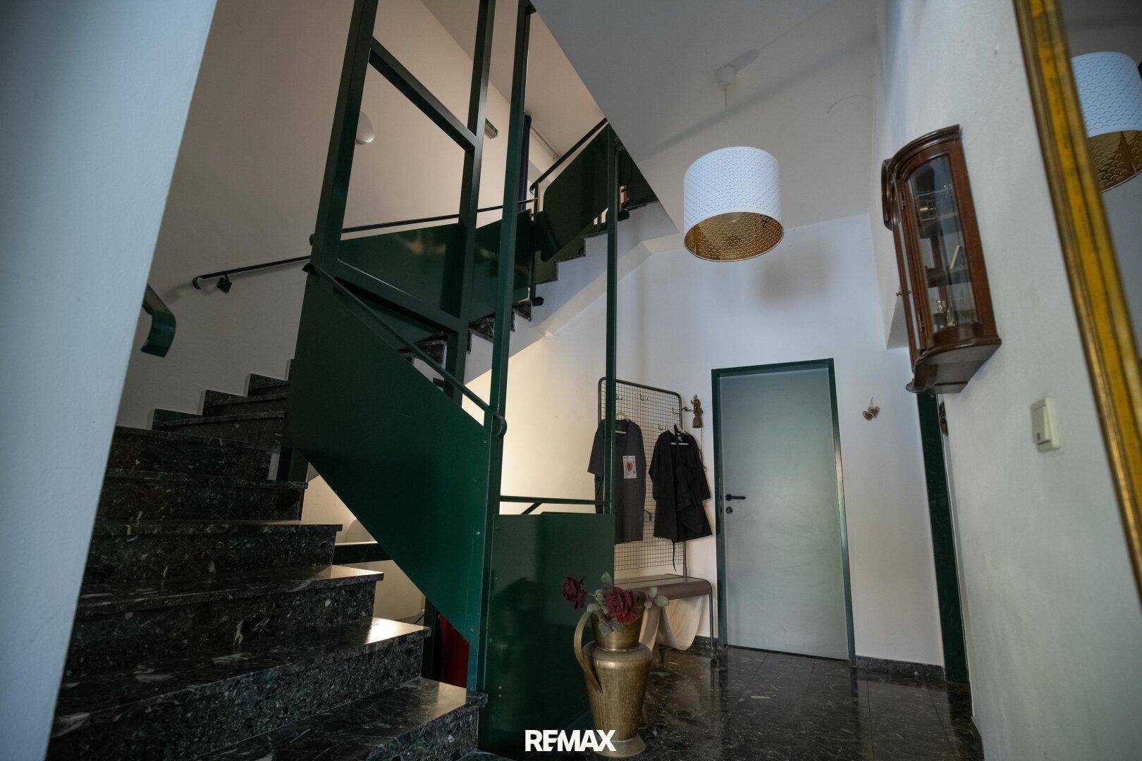 Treppenhaus mit dunklem Marmorboden und grünem Geländer, das zu den oberen Etagen führt.