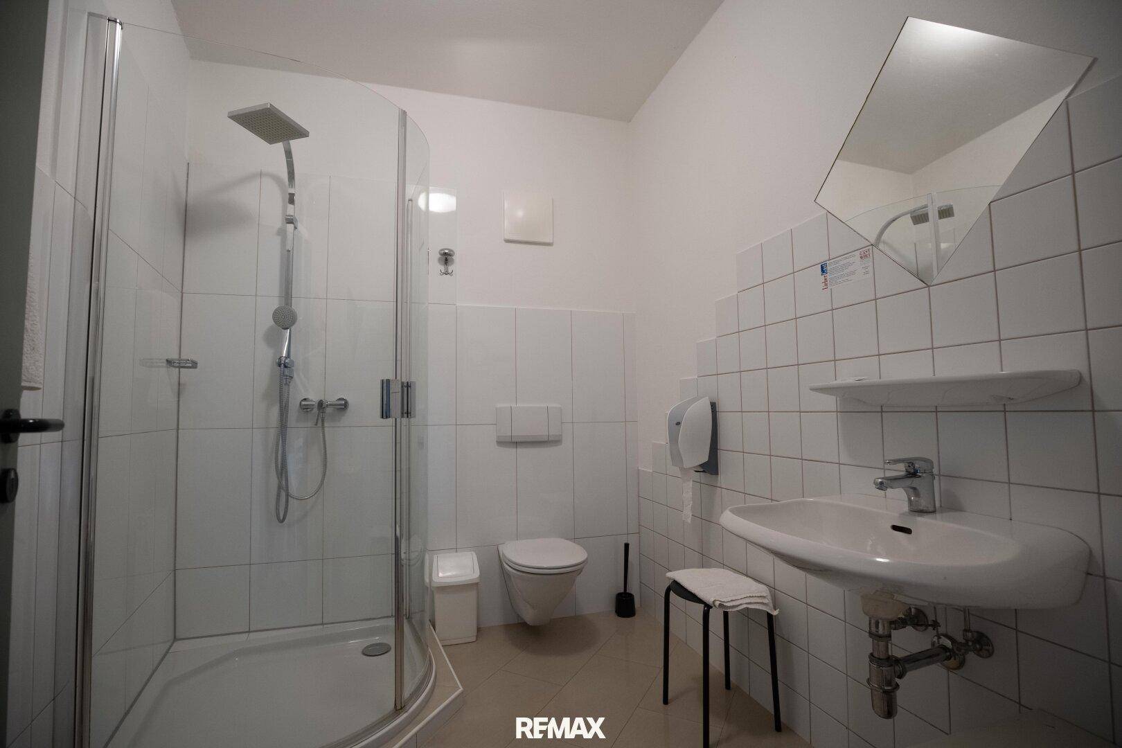 Helles Badezimmer mit Duschkabine, WC und Waschbecken, komplett gefliest.
