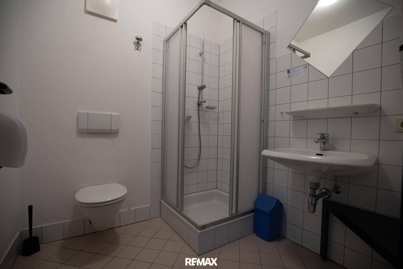 Helles Badezimmer mit Duschkabine, WC und Waschbecken, komplett gefliest.