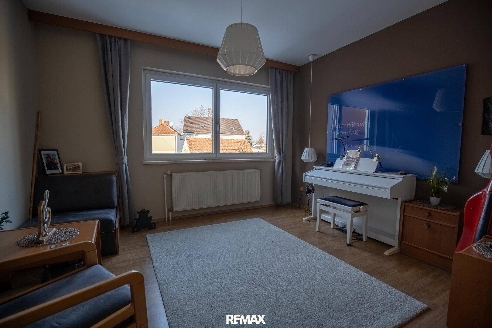 Helles Zimmer mit Klavier, Sitzgelegenheiten und Blick auf die Nachbarschaft.
