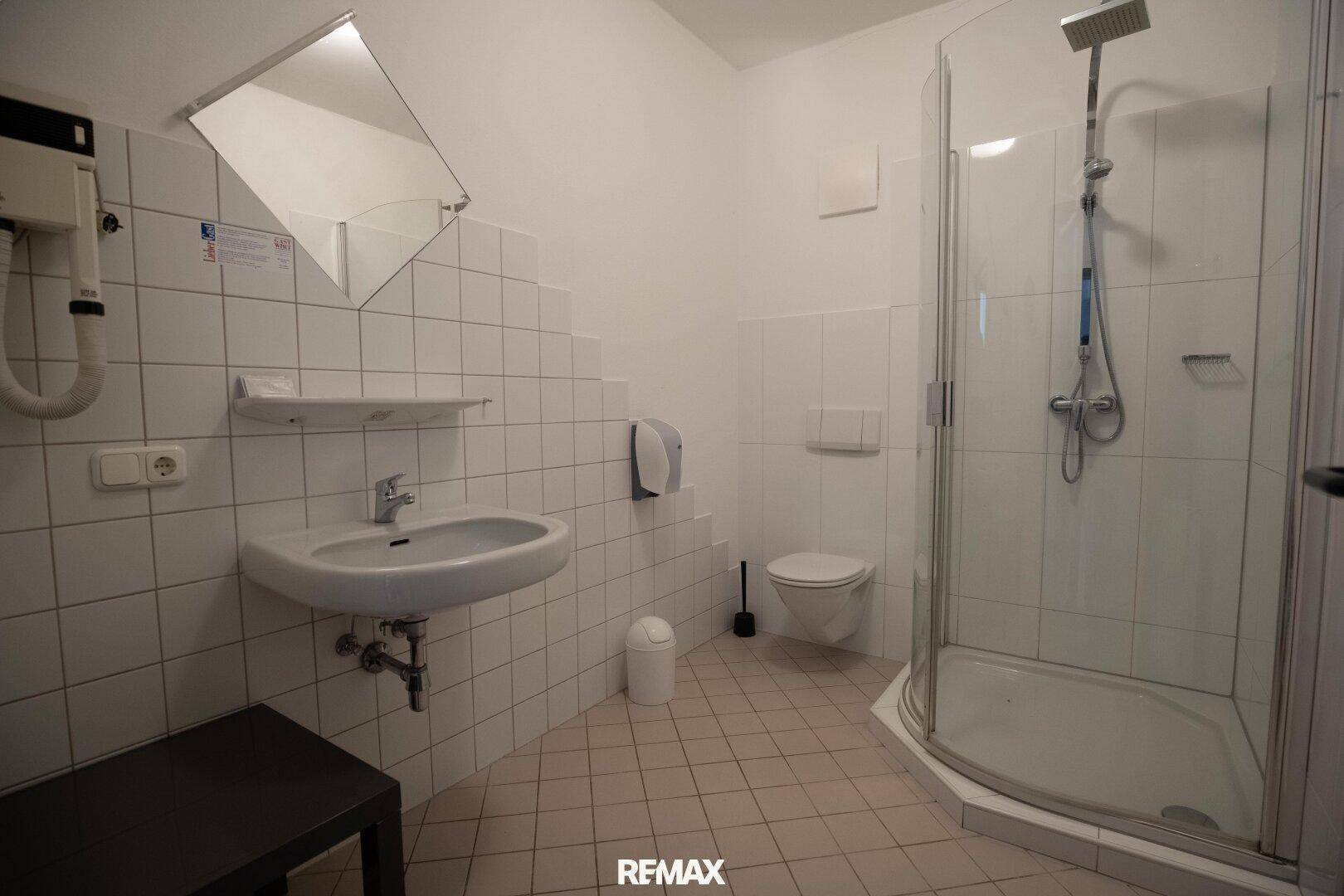 Funktionales Badezimmer mit Dusche, Waschbecken und weißen Fliesen.