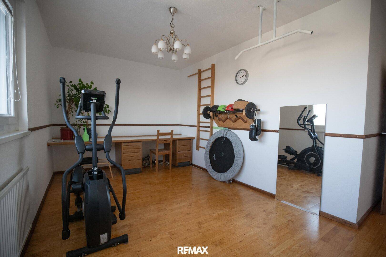 Vielseitiger Raum, eingerichtet als Fitnessbereich und Arbeitszimmer mit Holzboden und Fenster.