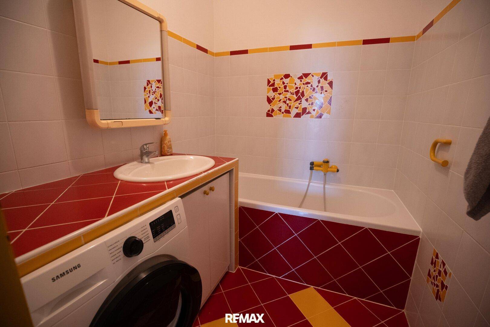 Badezimmer mit farbenfrohen Fliesen, Badewanne, Waschbecken und integrierter Waschmaschine.