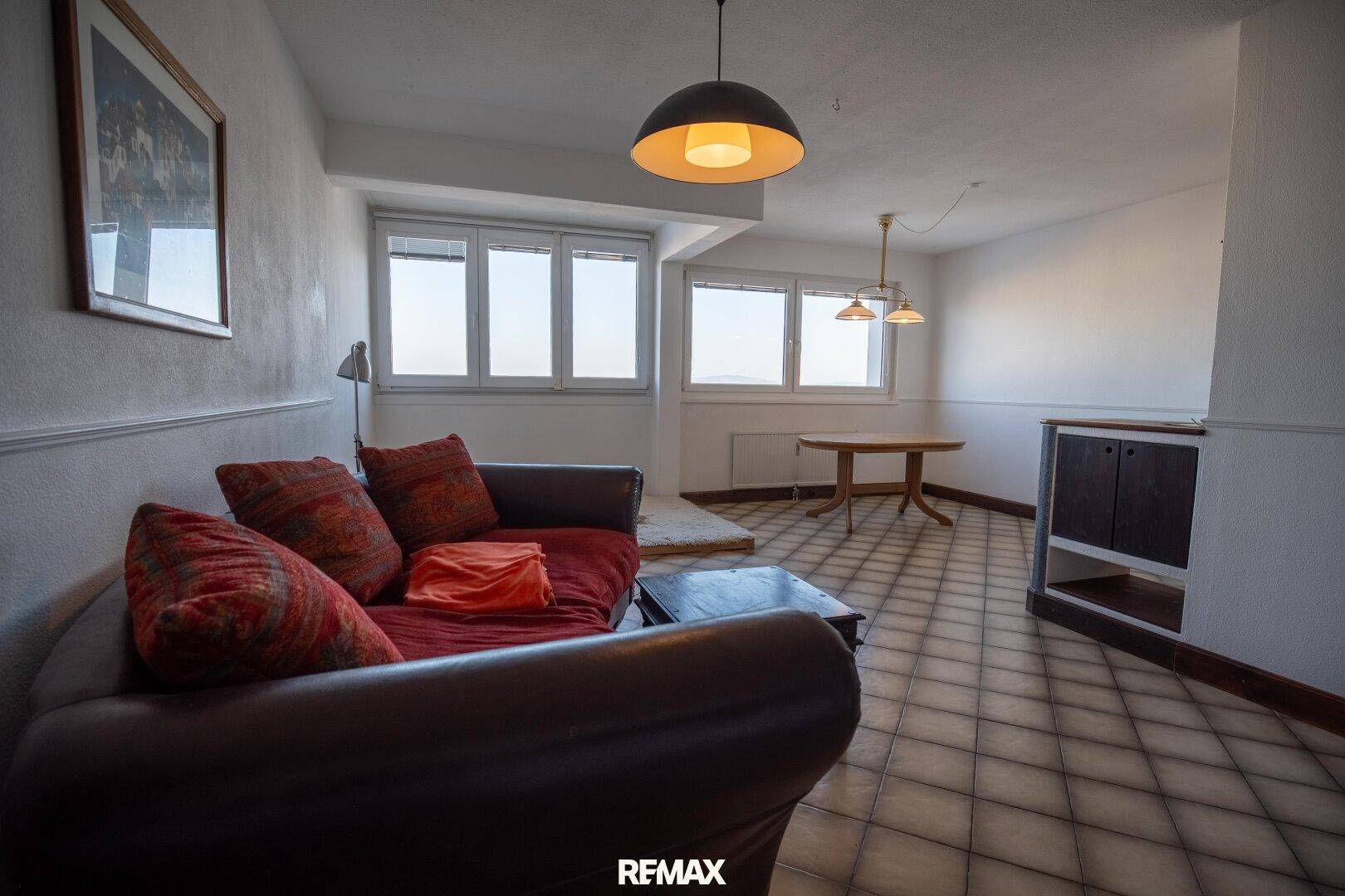 Helles Wohnzimmer mit gefliestem Boden, bequemer Couch und großen Fenstern mit Weitblick.