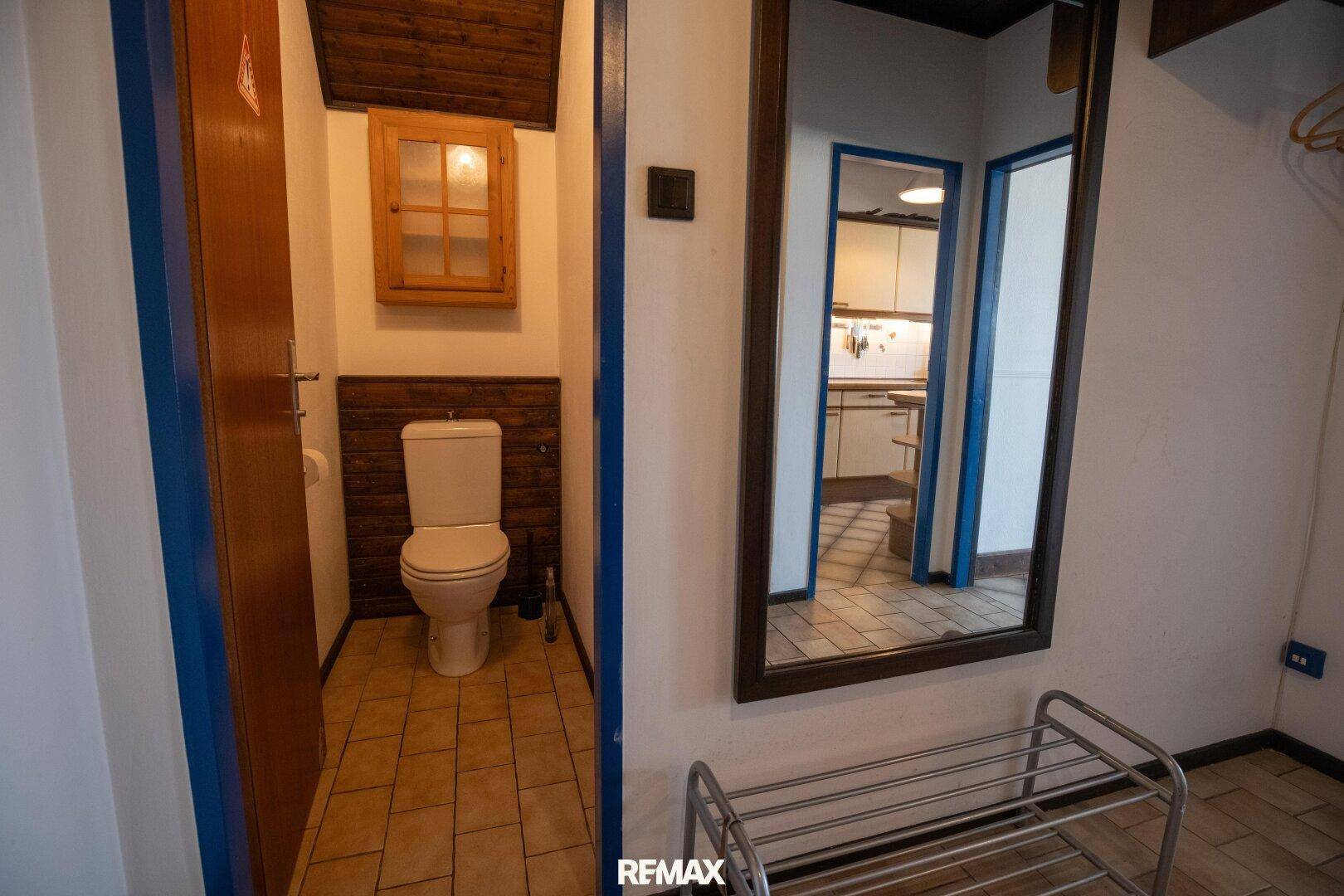 Separates WC mit Fliesenboden und einem großen Spiegel im angrenzenden Flurbereich.